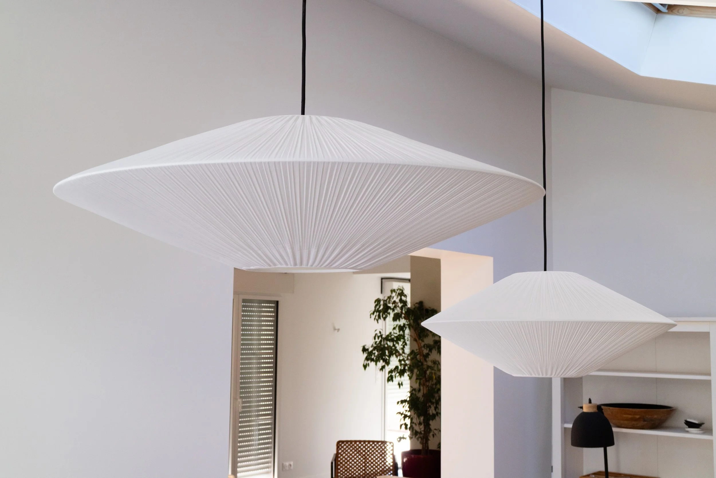 Suspensions lumineuses blanches en forme de parasol dans un intérieur moderne avec murs blancs, présence d'une plante verte et meubles.