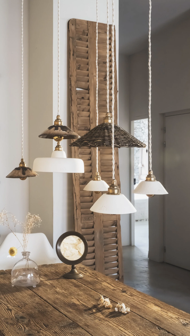 Suspensions luminaire de style vintage au-dessus d'une table en bois rustique, décor épuré avec un vase en verre et un petit miroir sur la table, mur blanc en arrière-plan.