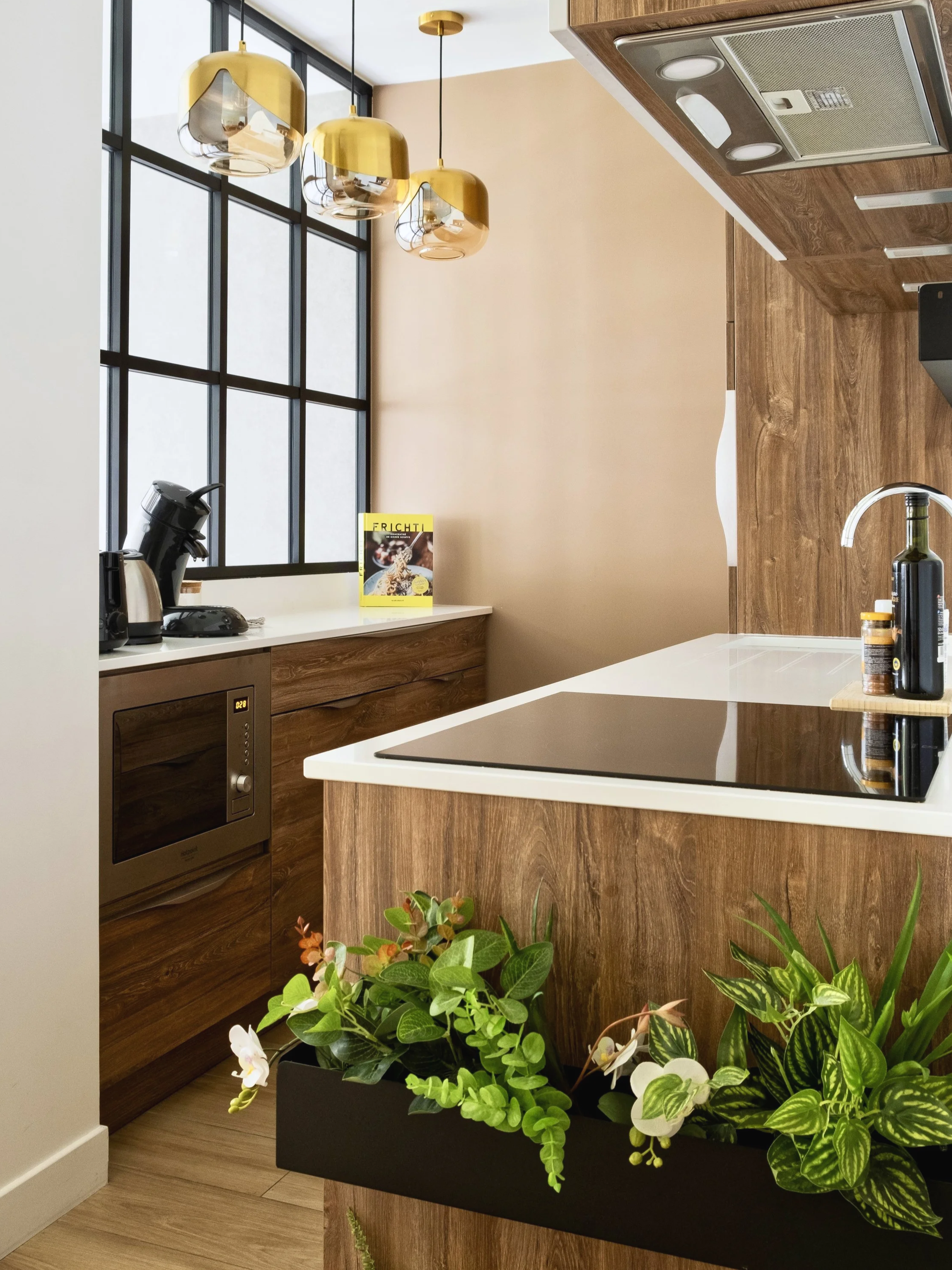 Une cuisine moderne avec un plan de travail en bois, des plantes en pot et un grand rideau en verre noir laissant entrer la lumière naturelle.