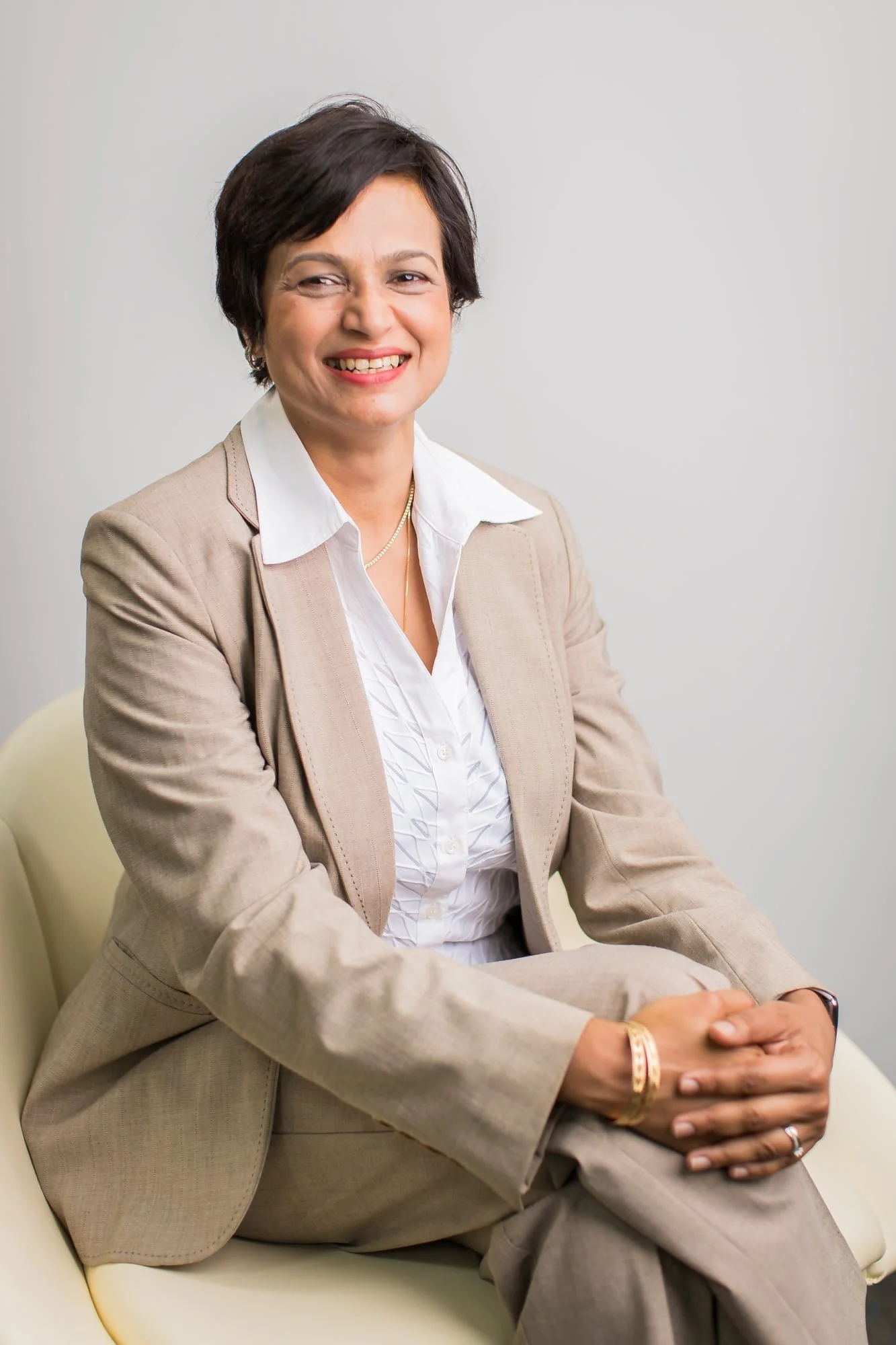 Business portrait of a woman in a beige blazer and white shirt seated at a desk.