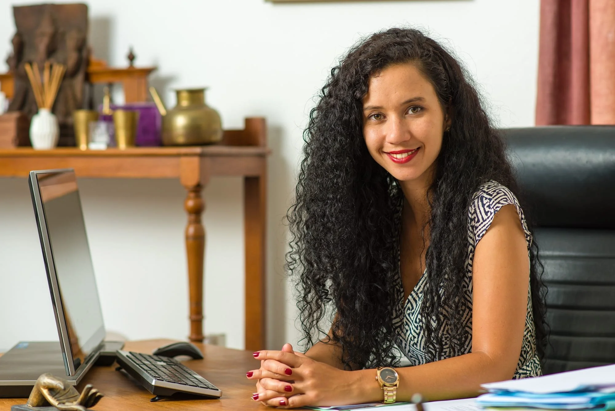 Environmental business portrait of a woman with long curly hair seated at a table in a warm interior.