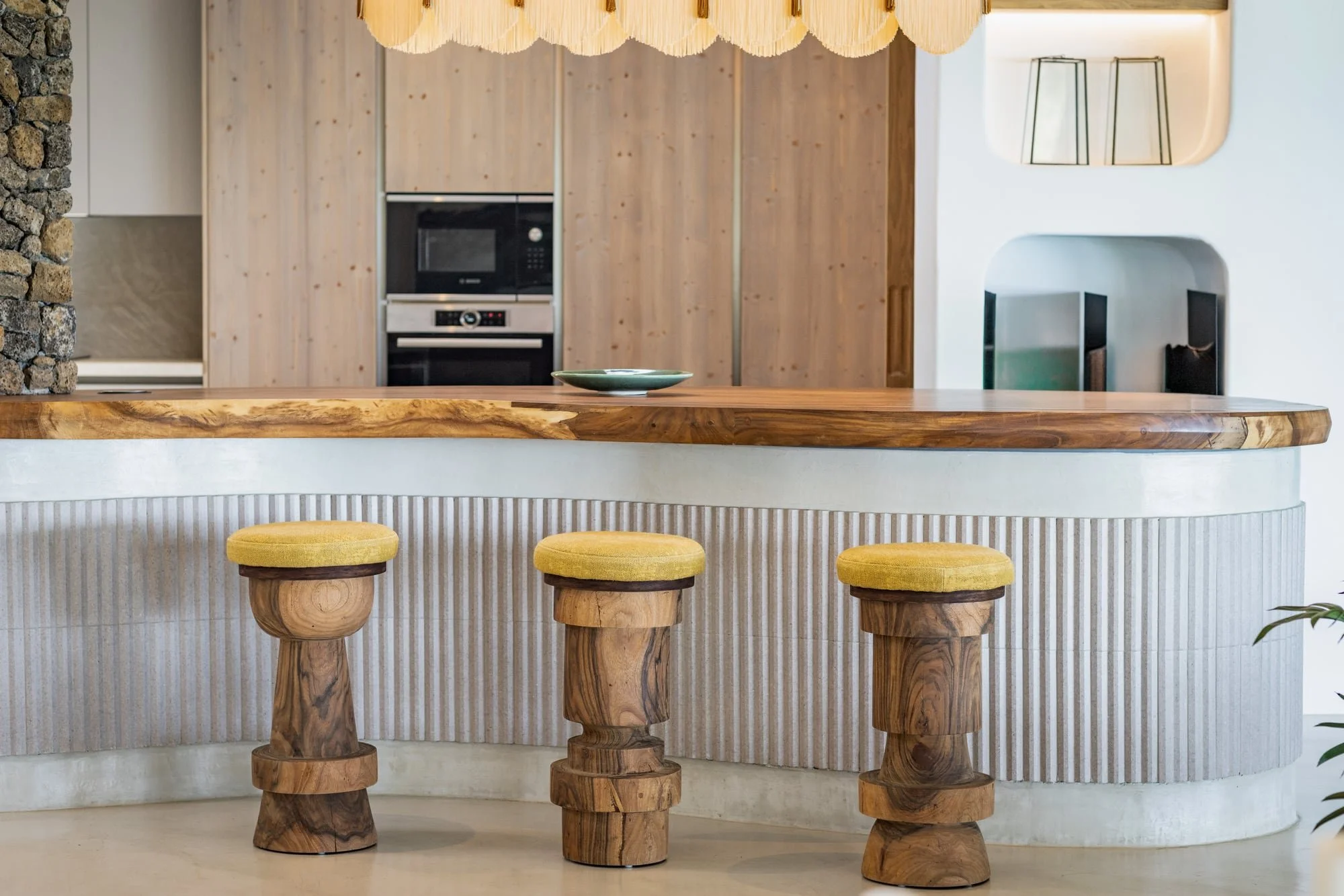 Muse Villa — kitchen island with timber, stone and sculptural cabinetry.