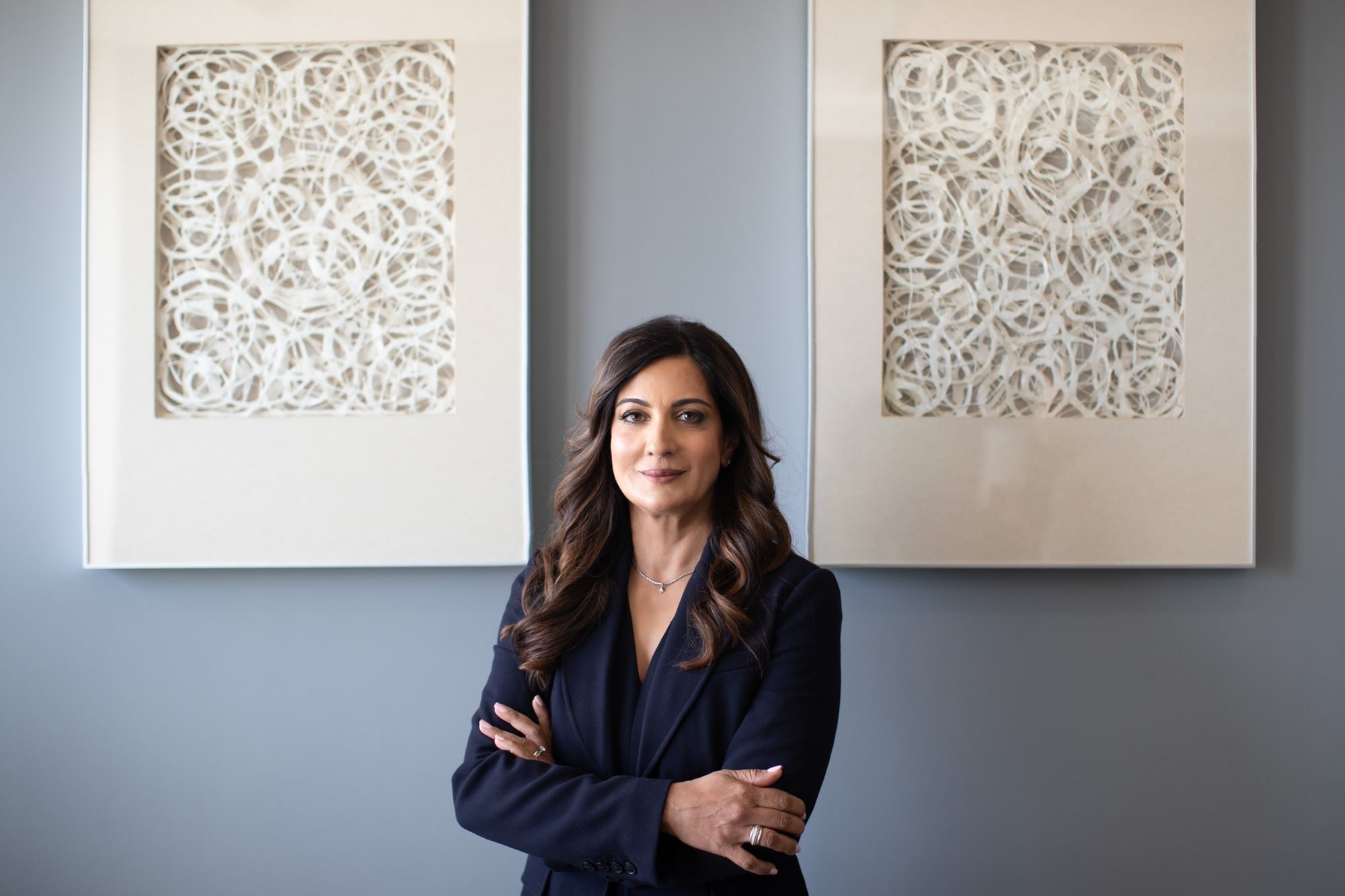 Corporate portrait of Sharmila Harel in a dark blazer posed beneath framed artwork.