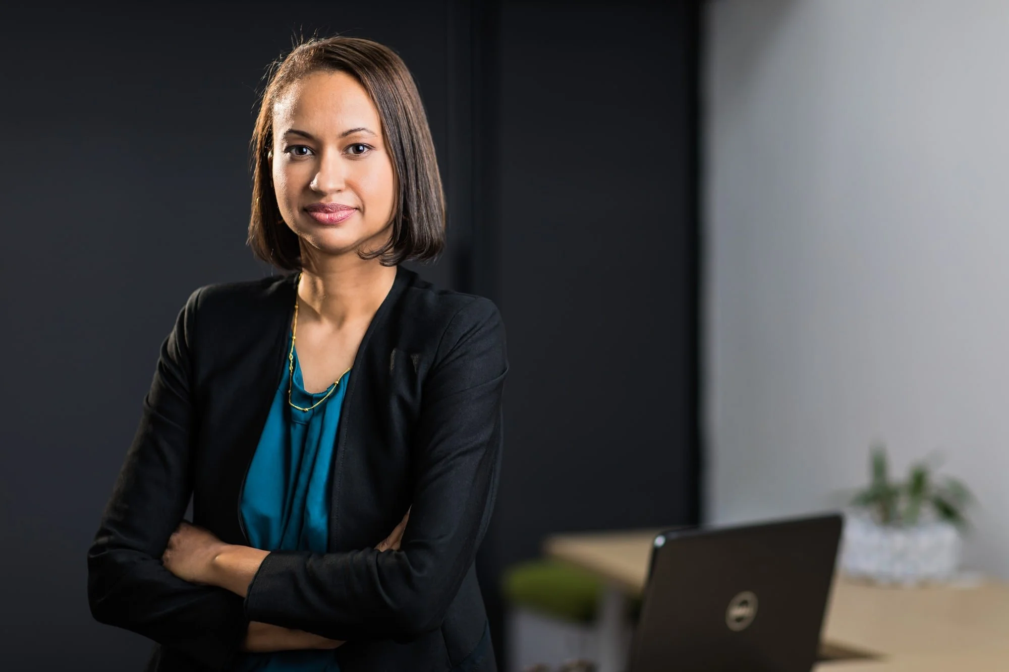 Close-up business portrait of a woman in a dark blazer against a softly lit background.