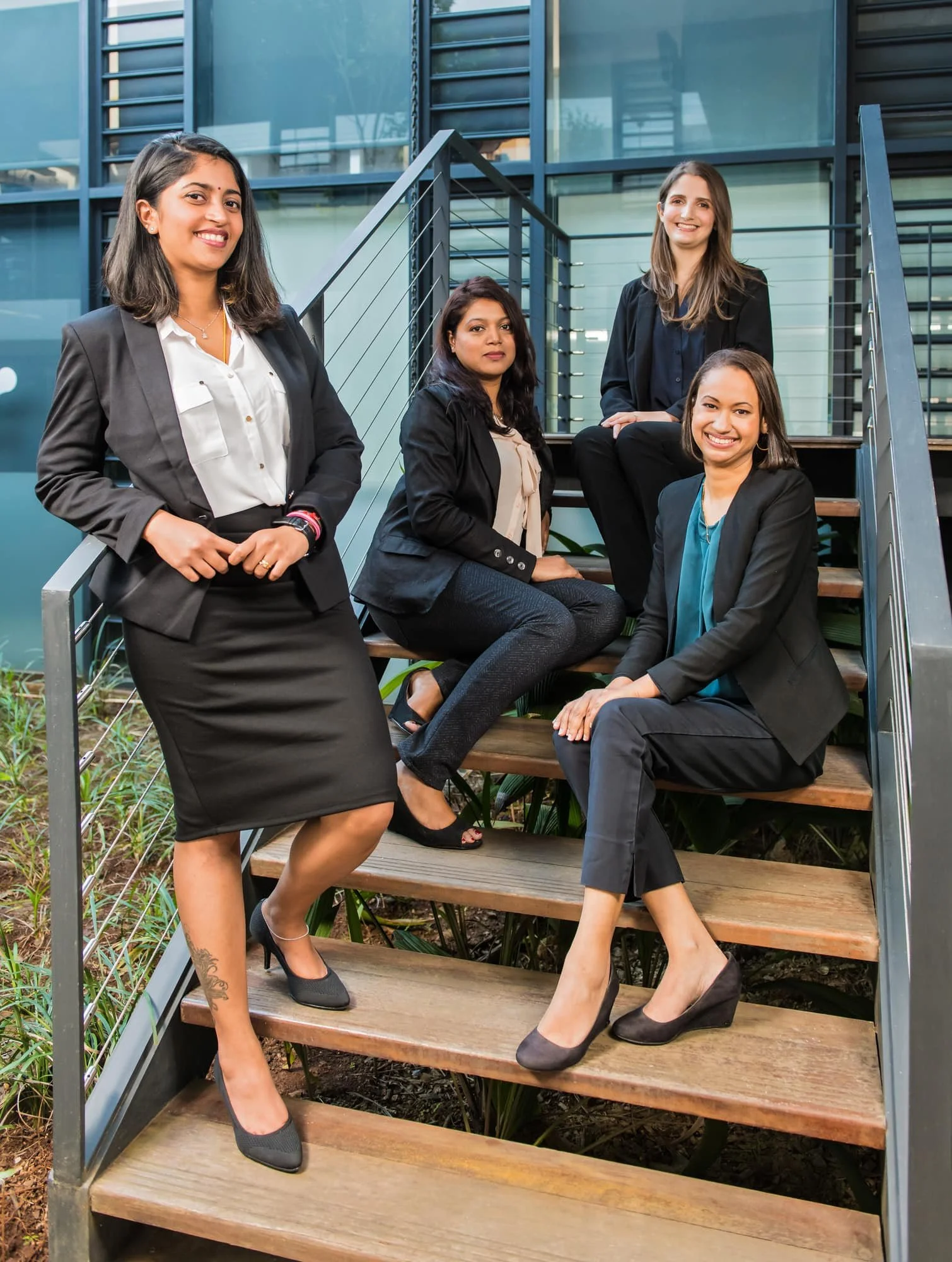 Corporate team portrait of women posed on steps outside a contemporary workplace.