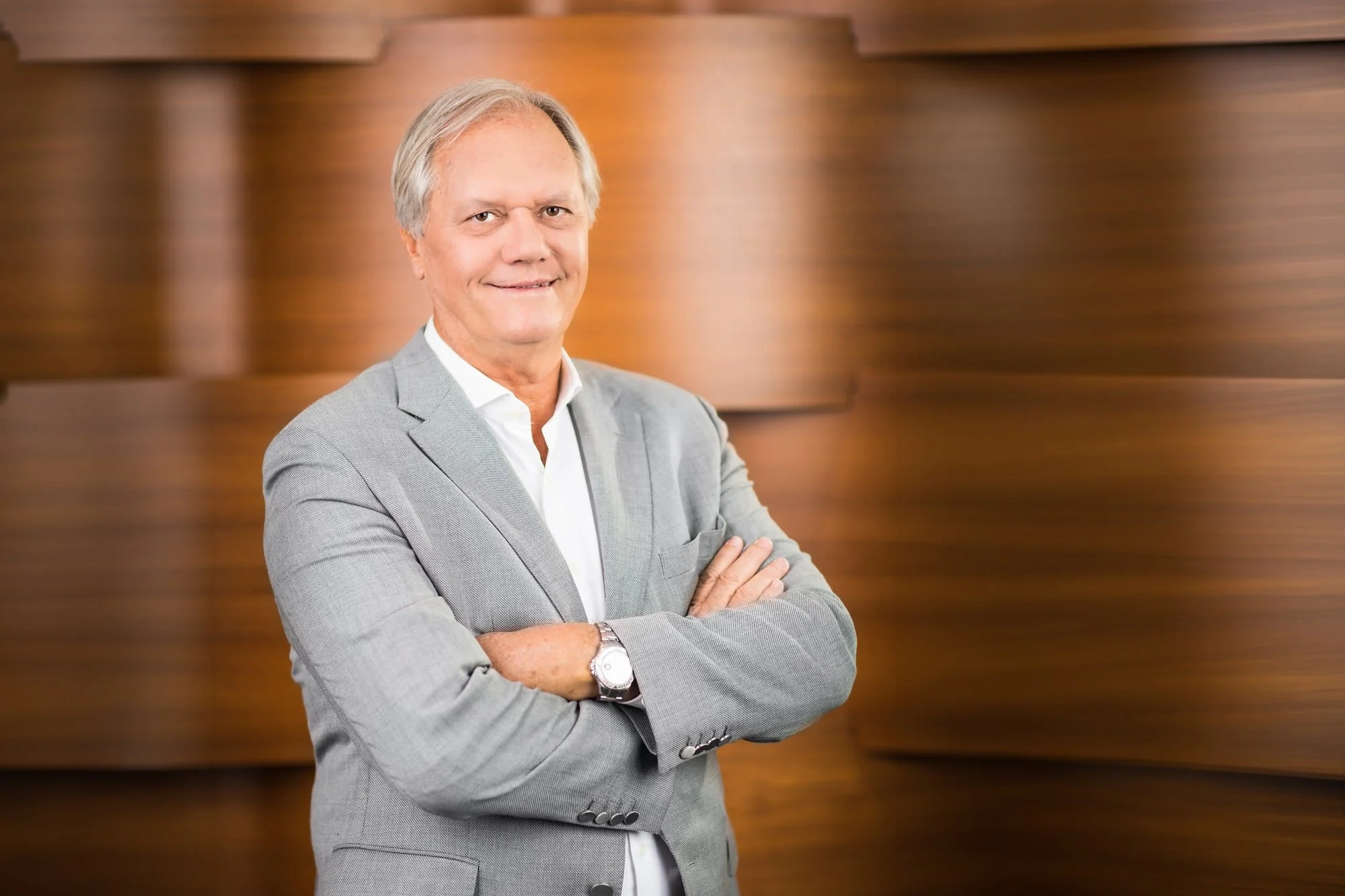 Corporate portrait of Thierry Lagesse in a grey checked blazer with folded arms against a warm wood interior.