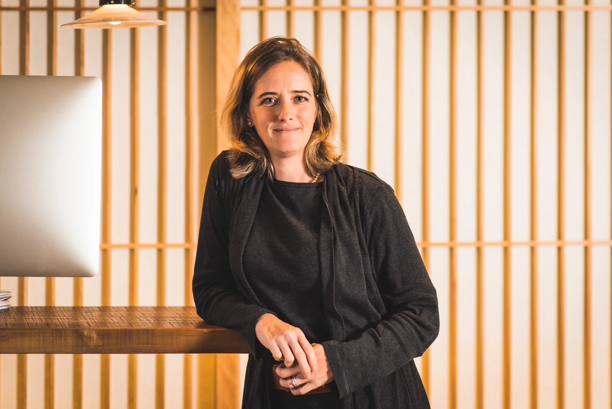 Professional portrait of Axelle Mazery in a black blouse beside a vertical timber screen.