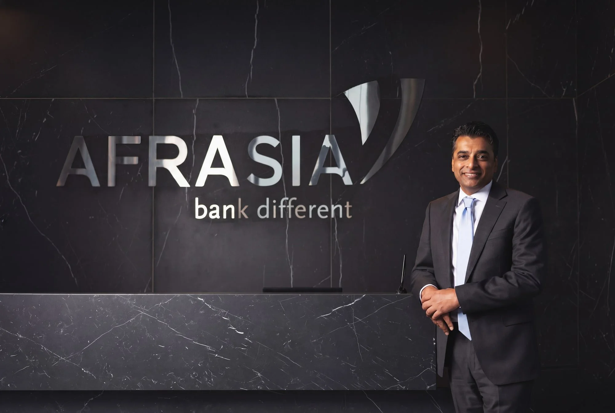 Professional portrait of a man in a suit standing beside an AfrAsia Bank sign.