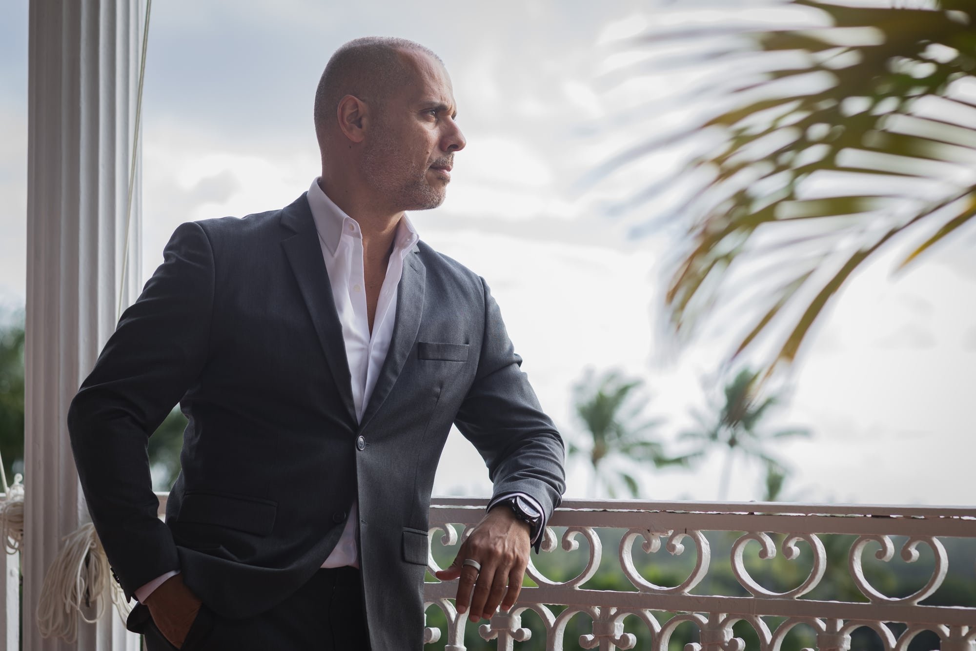 Environmental portrait of Samer Kassem in a suit on a balcony with palm trees in the background.