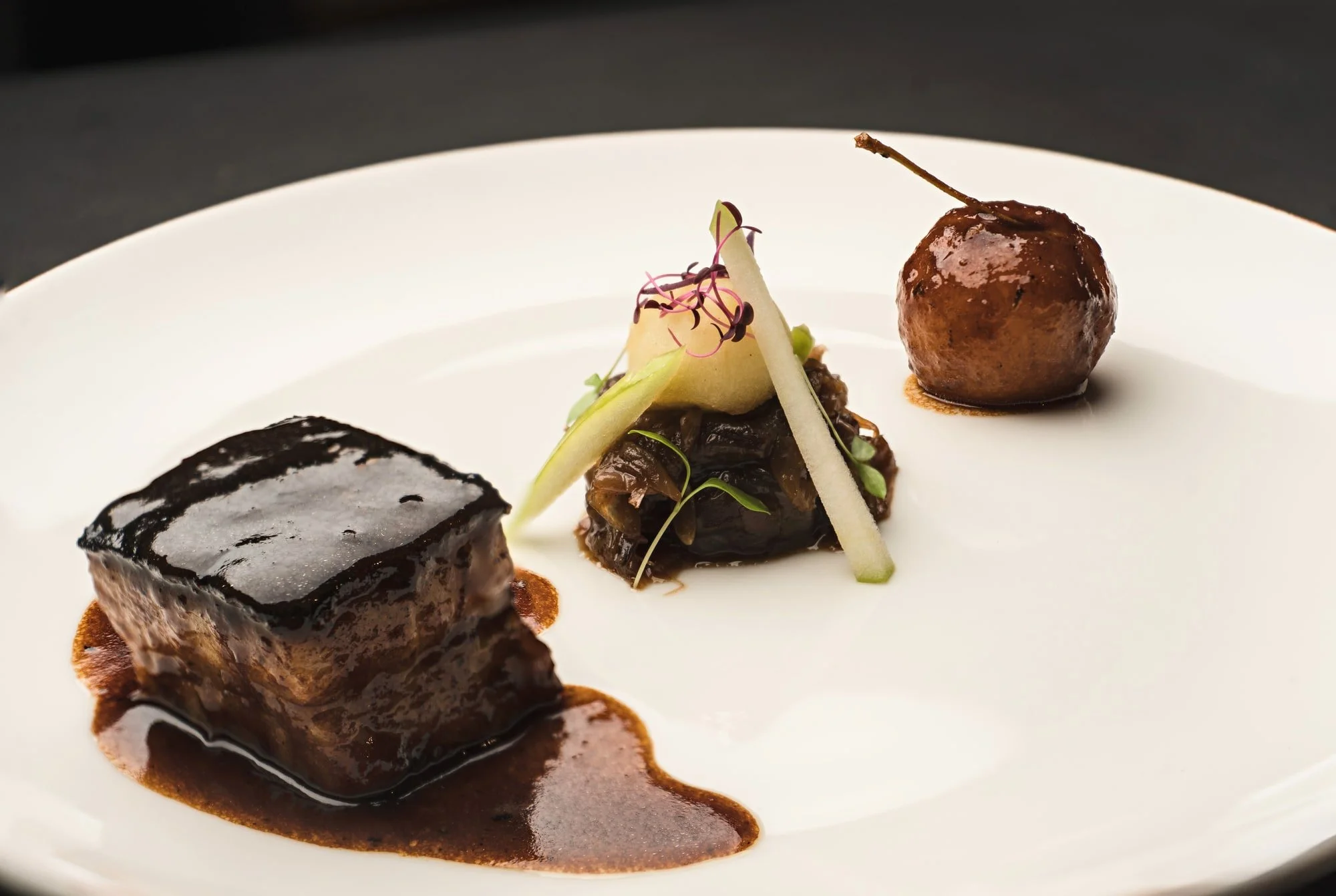 Glazed meat with seasonal vegetable garnish on a contemporary fine-dining plate.