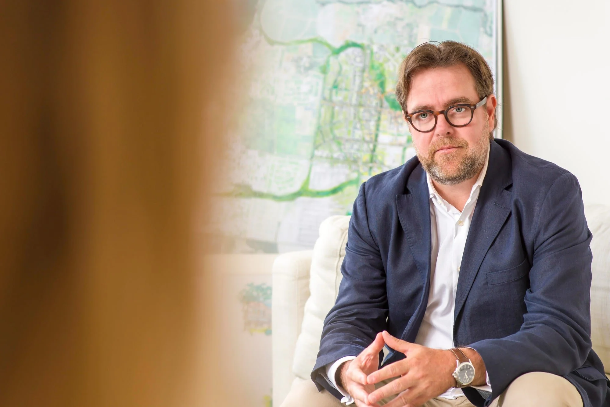 Business portrait of Thierry Sauzier wearing glasses and a navy blazer, seated beside a bright window.