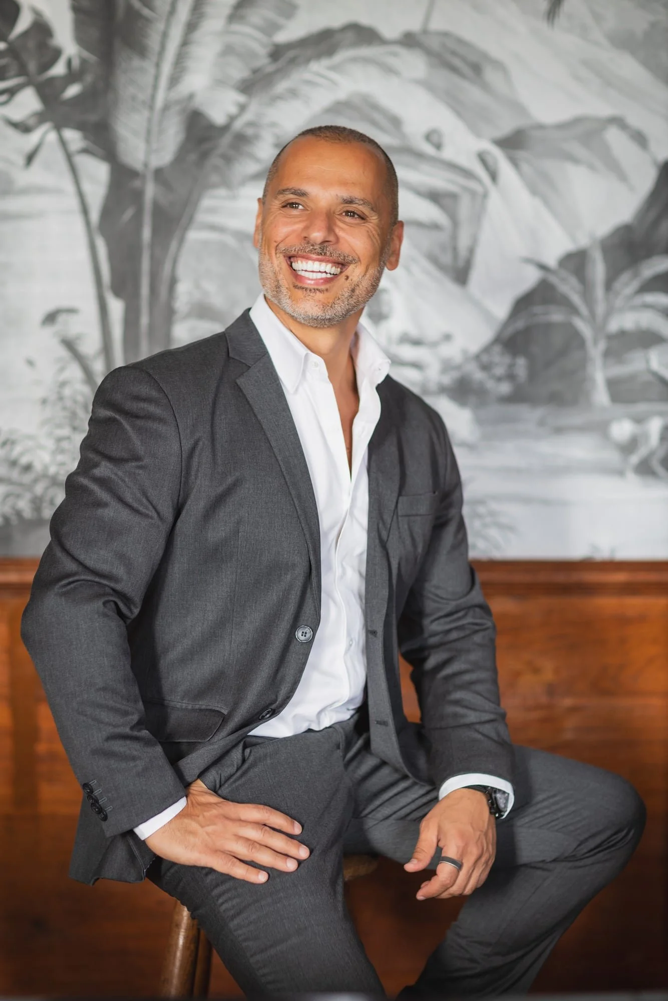 Business portrait of Samer Kassem in a grey suit seated on a sofa beside a window.