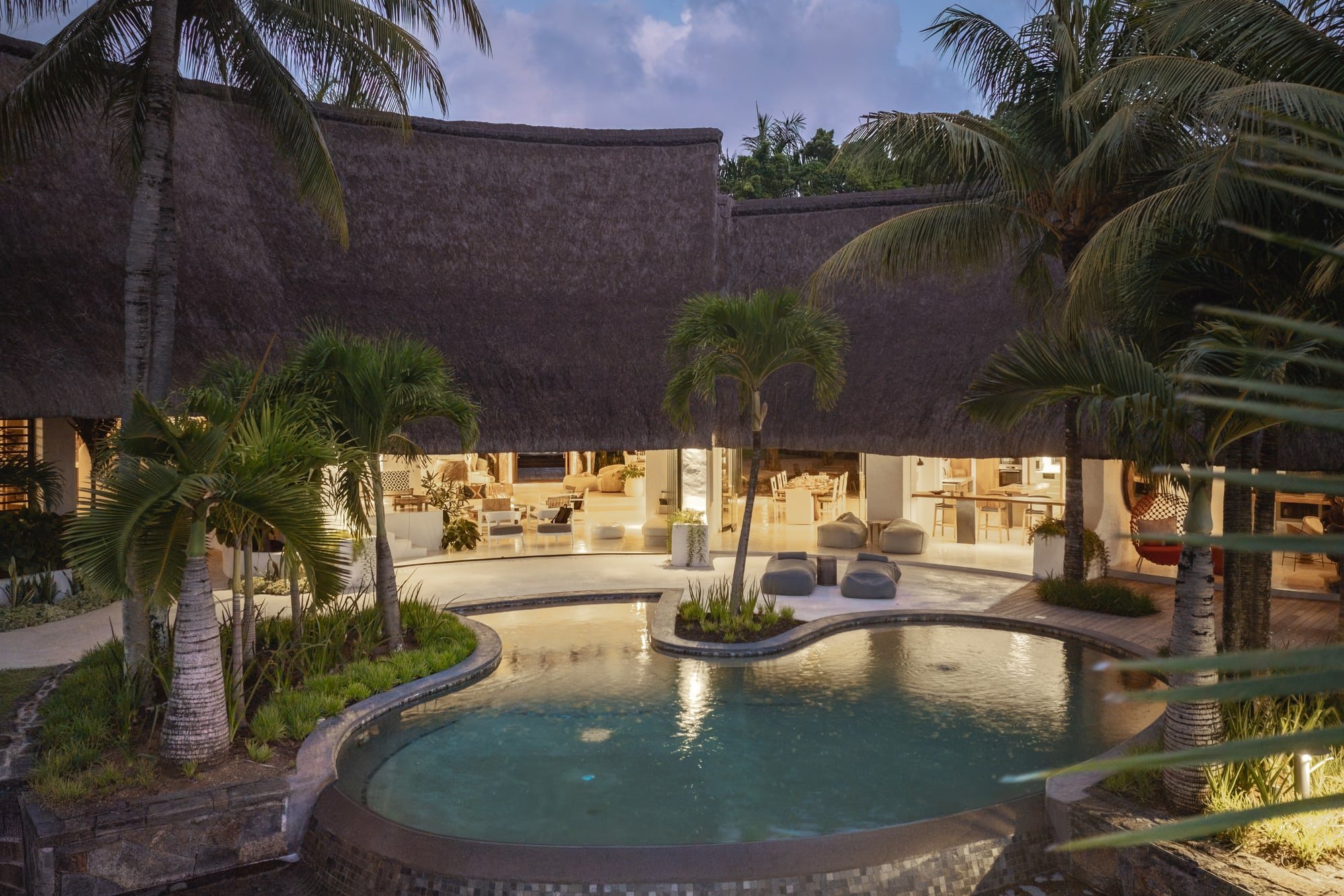 Muse Villa — curved pool and thatched architecture at dusk.
