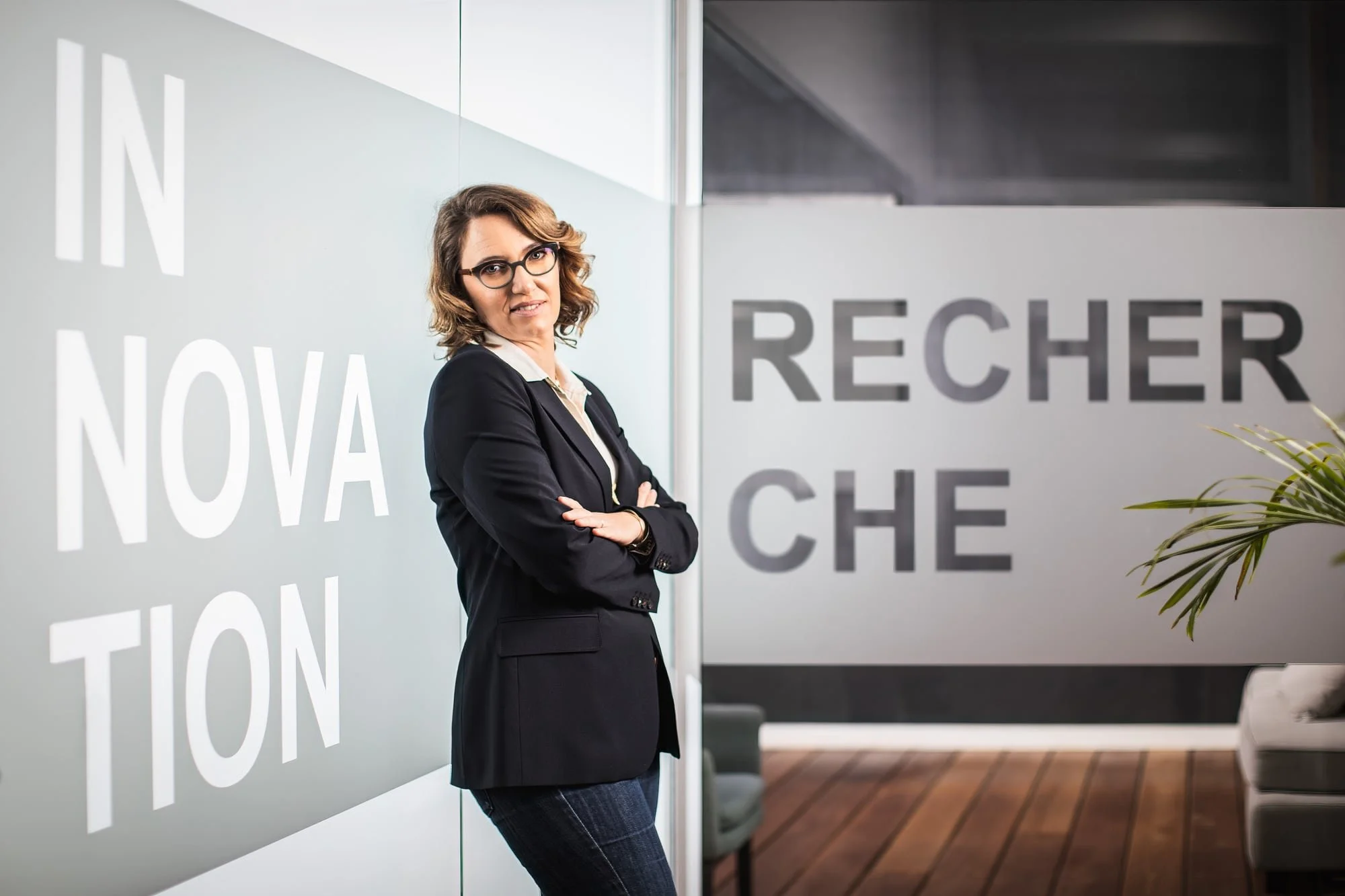 Professional portrait of a woman in a dark suit with folded arms against a graphic office wall.