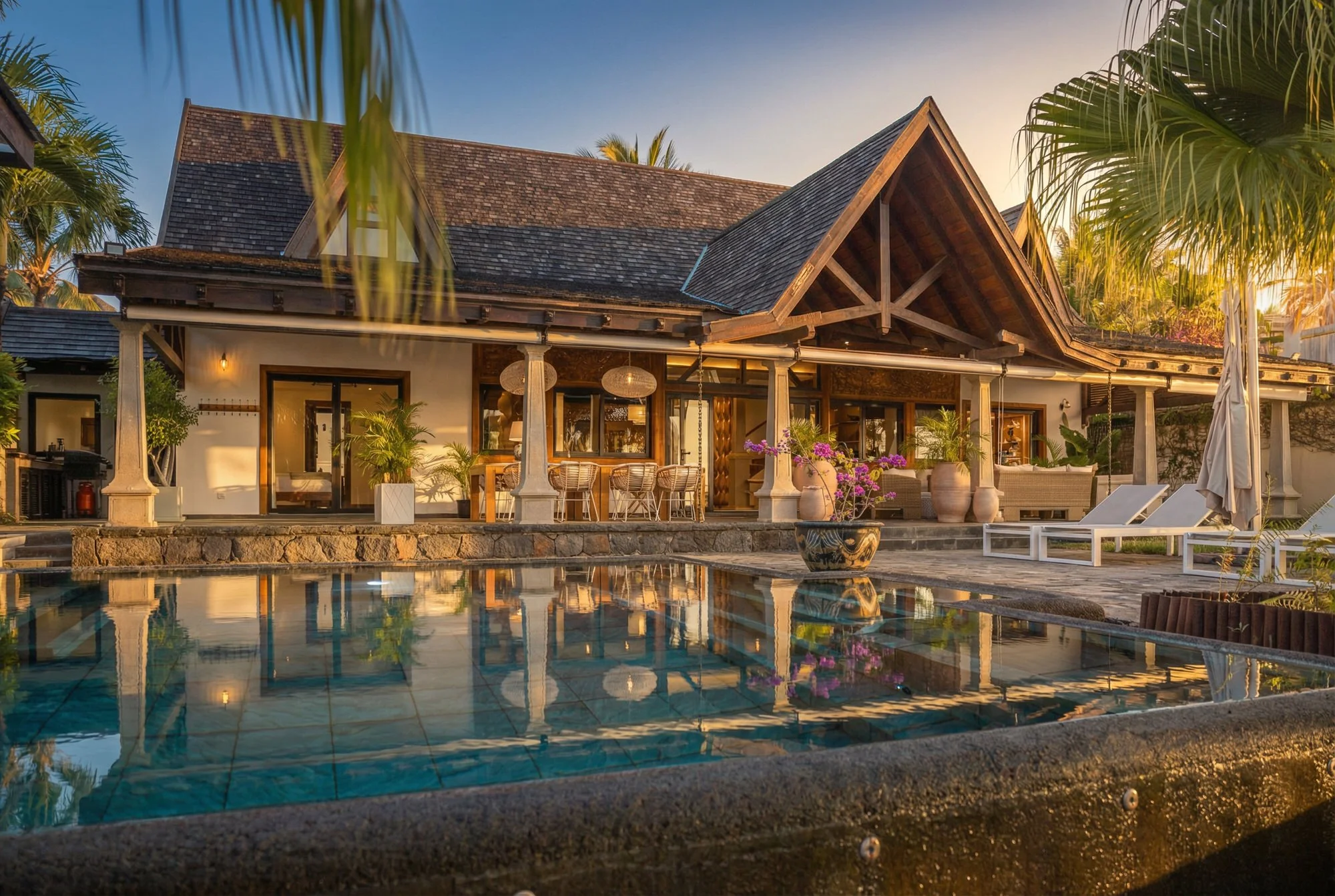 Matahari Villa, Mauritius — timber-roofed architecture reflected in a pool at dusk.