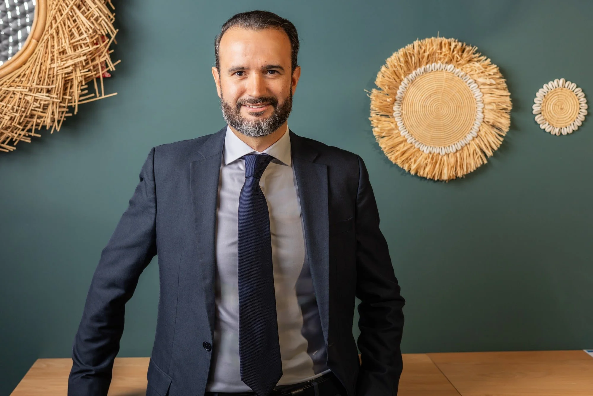 Business portrait of Jonathan Wienand in a dark suit and tie against a deep green wall with decorative artwork.