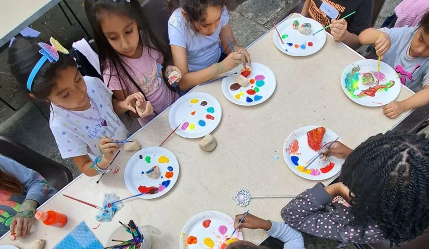 Children painting rocks at a table outdoors.