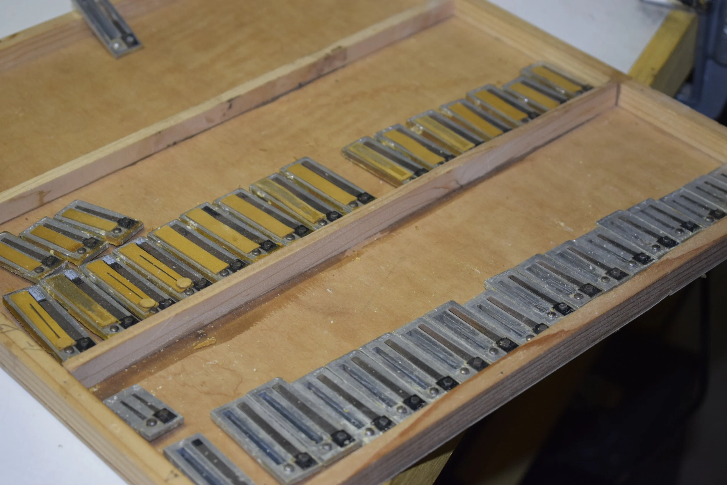 Una scatola di legno con vari pezzi metallici e dorati disposti ordinatamente.