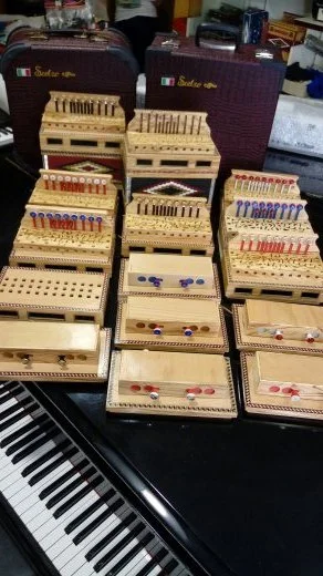 Set di strumenti musicali in miniatura, inclusi xilofoni e maracas, disposti in scatole di legno su un piano, con valigette viola e dettagli di un pianoforte in primo piano.