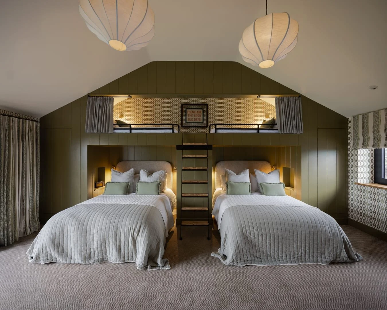 A bedroom with two beds in the foreground and a lofted bed above, connected by a ladder, with cozy decor and patterned wallpaper.