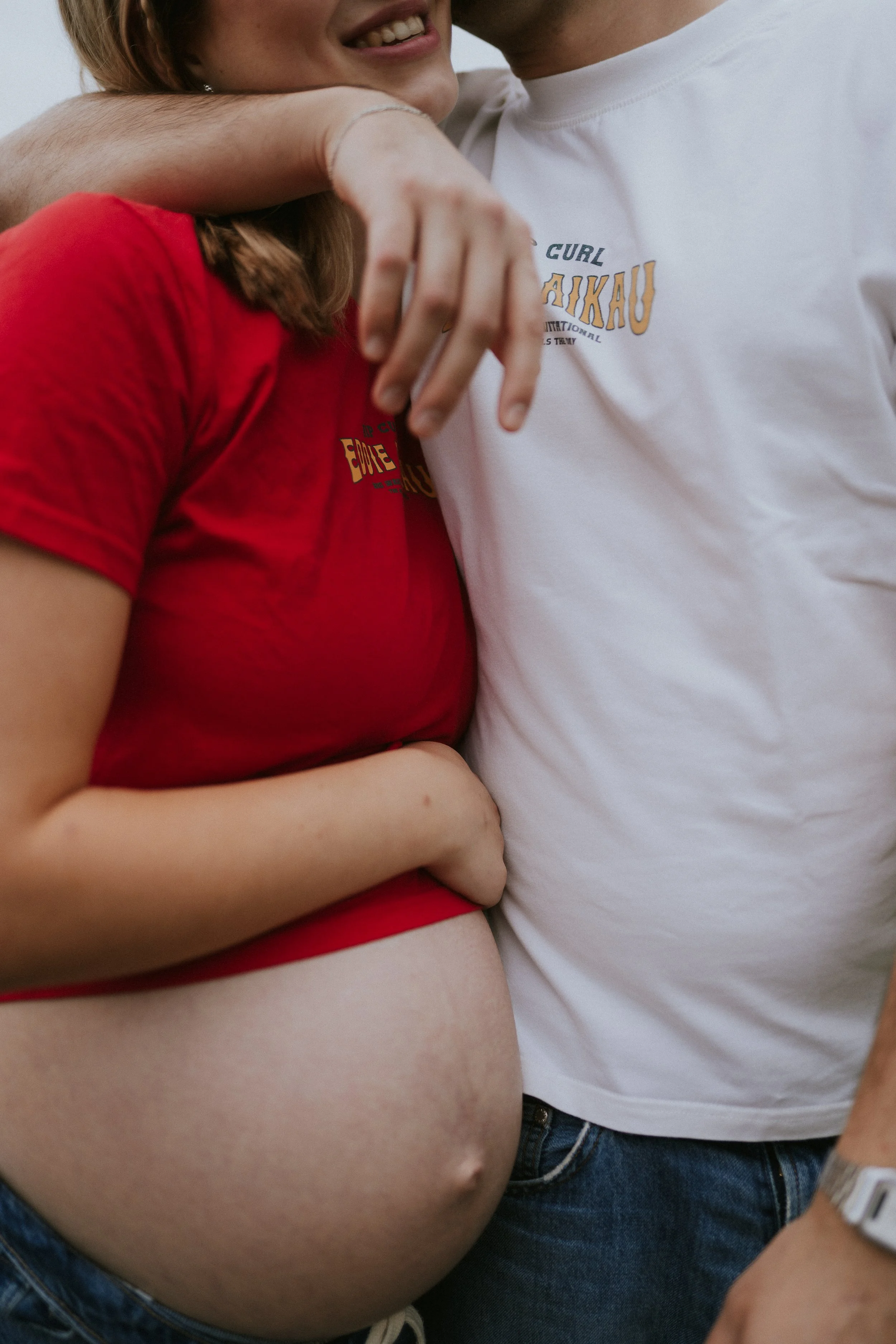 Nahaufnahme von zwei Personen, die sich eng umarmen, mit einem Fokus auf ihren Oberkörper und Arme. Eine Person trägt ein rotes T-Shirt, die andere ein weißes T-Shirt.