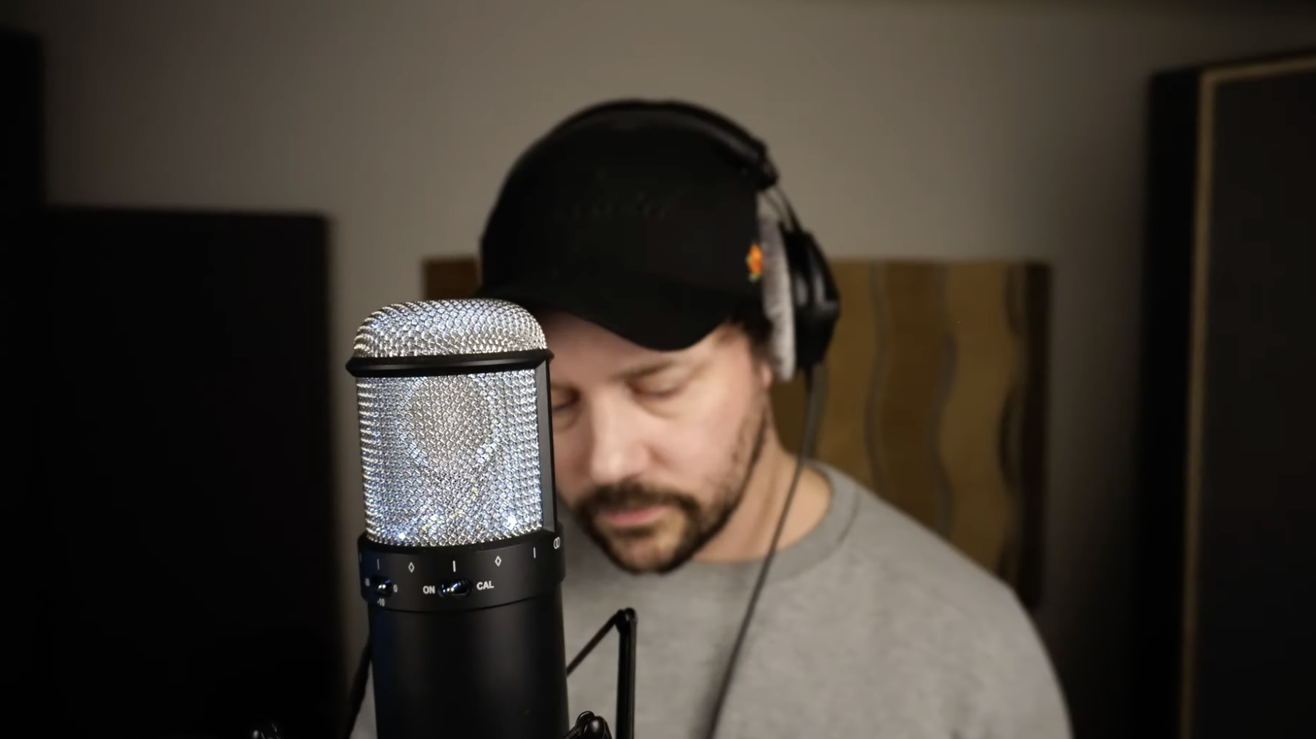 Man i studioljudinspelning, nära mikrofon, med hörlurar, med ögon stängda eller tittar nedåt.