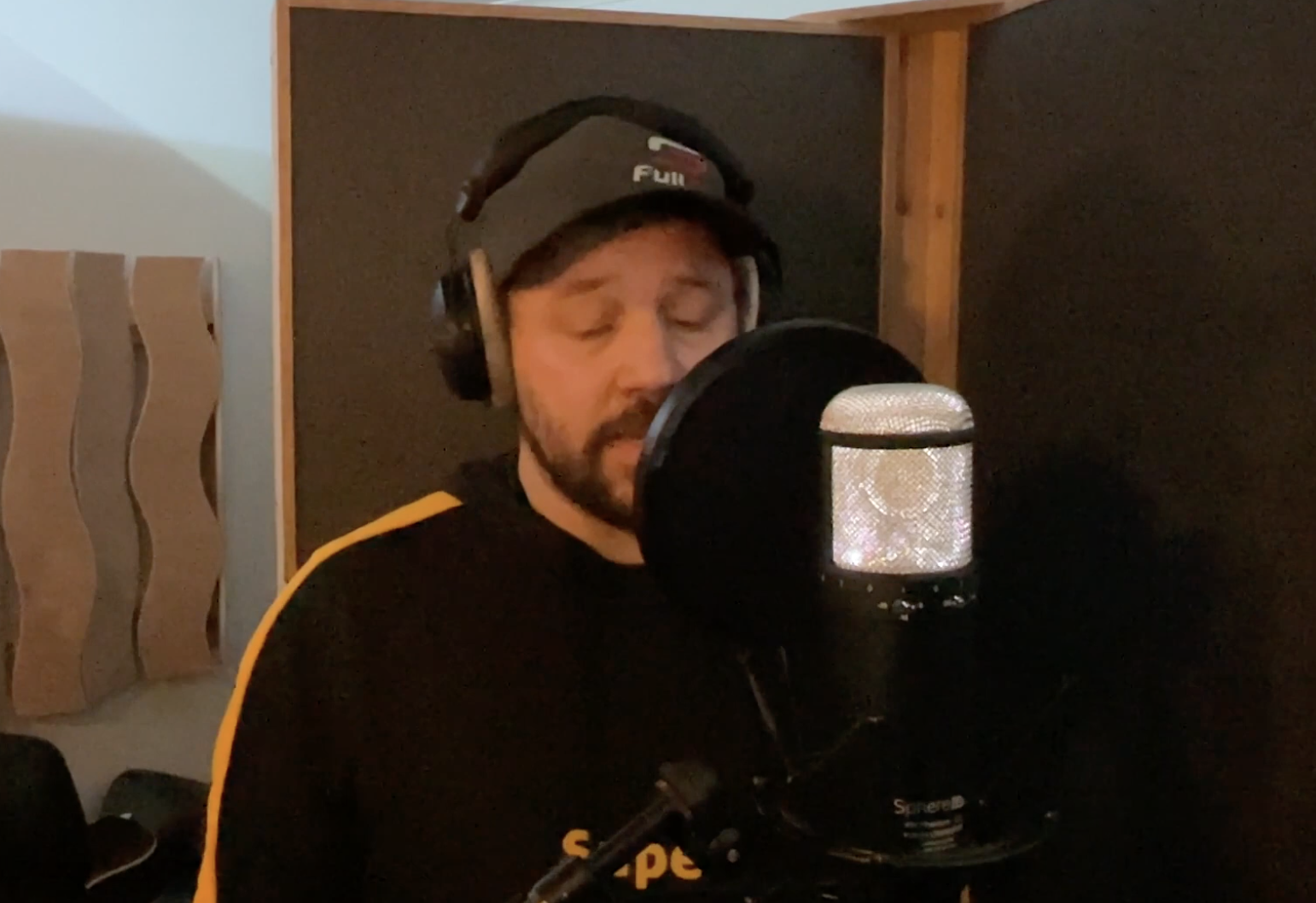 Man med mössa och hörlurar som sjunger eller pratar i en mikrofon i en inspelningsstudio.