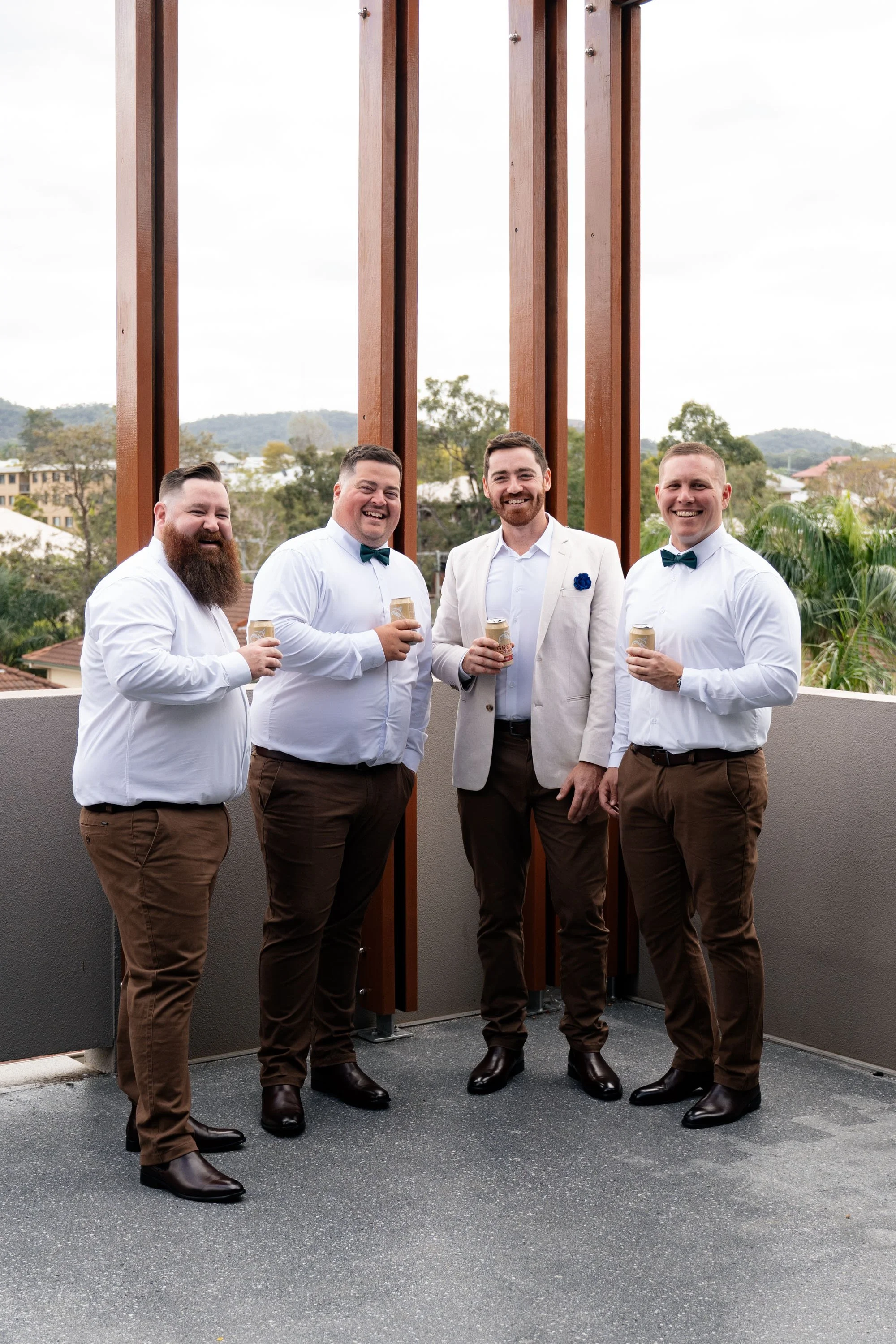 Groom Thomas and his groomsmen looking at Brisbane wedding photographer Whistler, holding beers and sharing a fun, carefree moment during the wedding day.