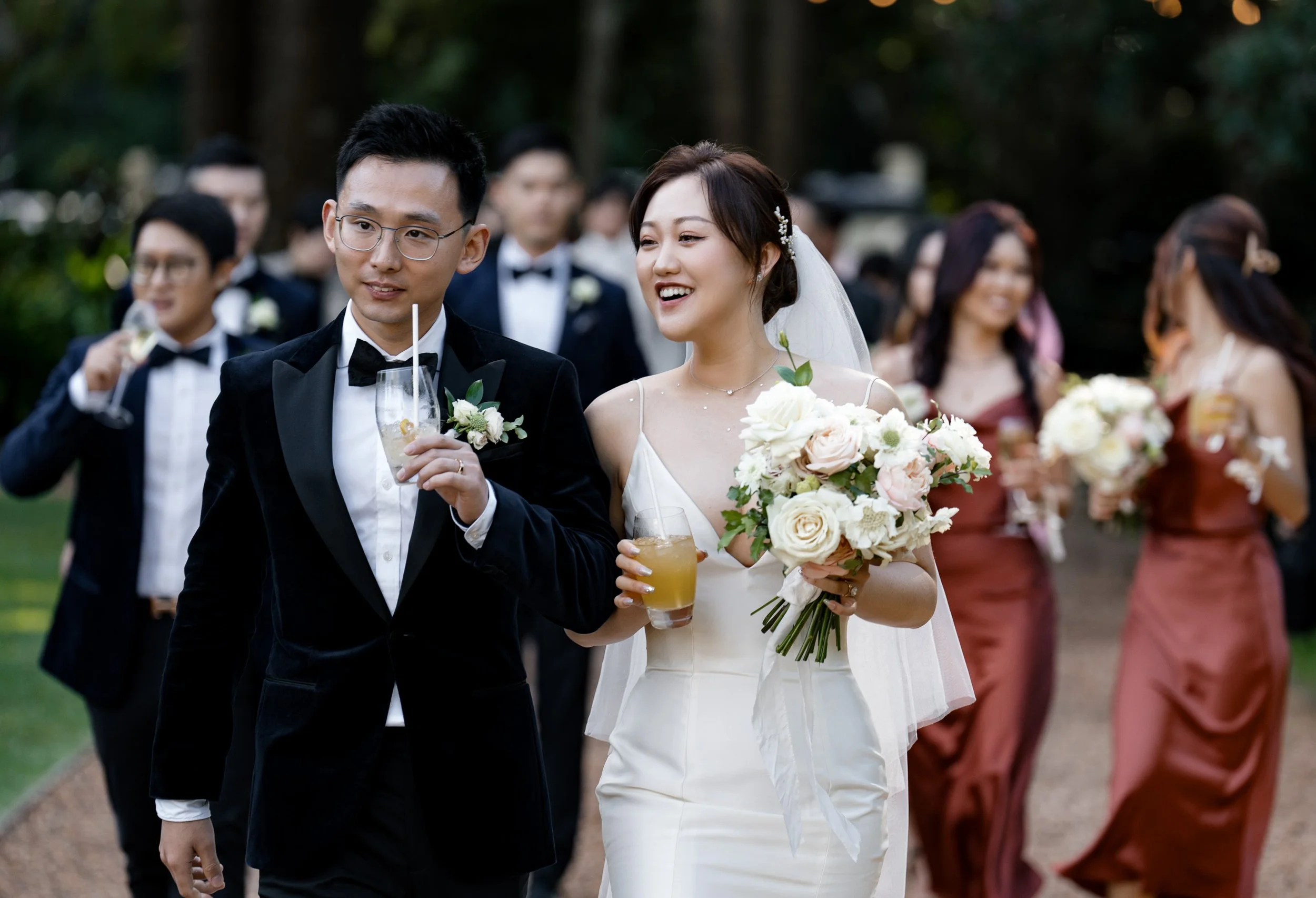 bride and groom holding drinks leading bridal party walking