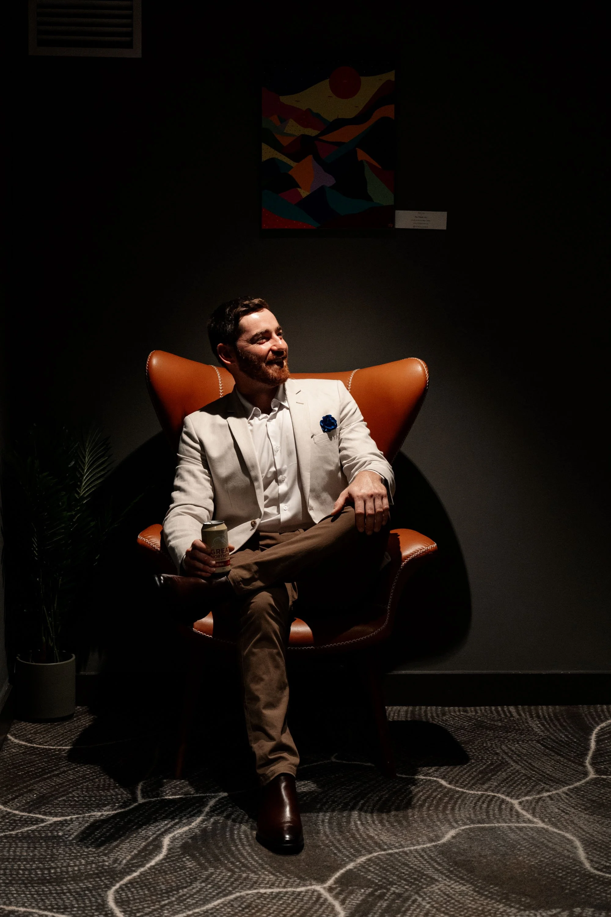 Groom sitting on a chair, looking up with a thoughtful or eager expression, capturing a quiet yet significant moment before the wedding