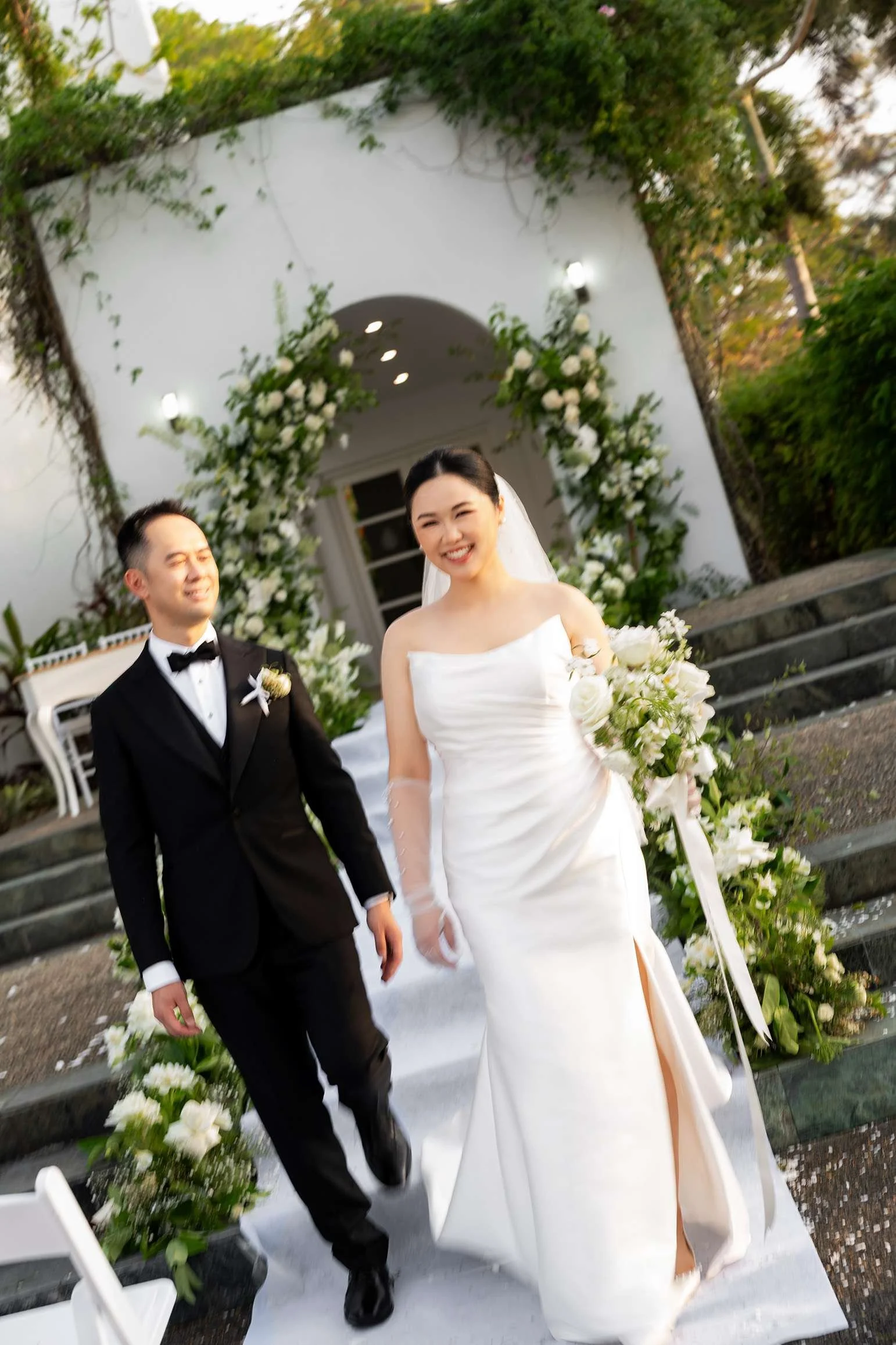bride Wendy smell to the Brisbane wedding photographer Whistler Li while holding a flower and groom Alex walking behind her