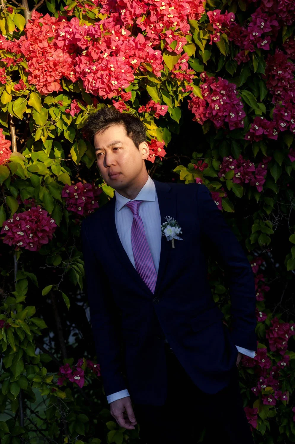 The groom Eric stands among a bed of flowers, with warm sunlight gently illuminating his face.