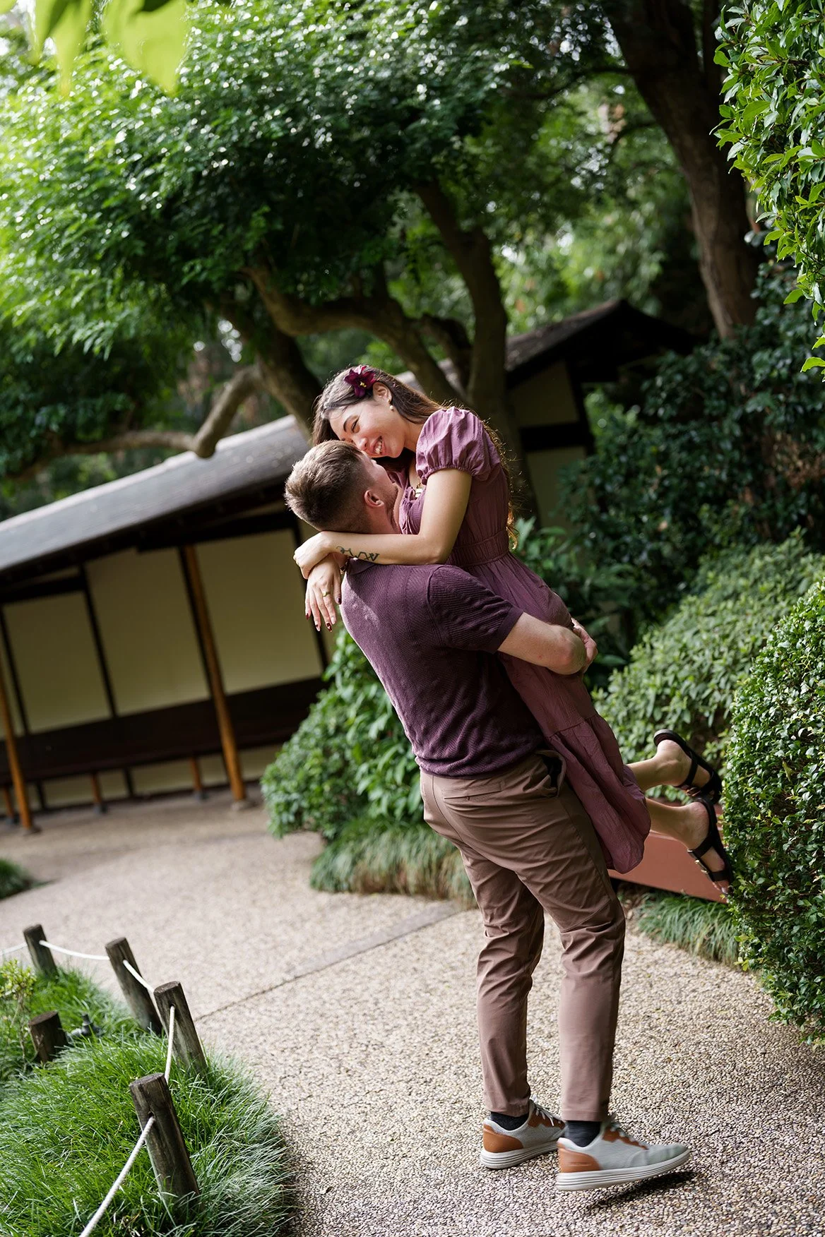 Kyle holding Ruby up and try to kiss her, her hand on his shoulder in Japanese garden Brisbane Botanic Gardens Mt Coot-tha