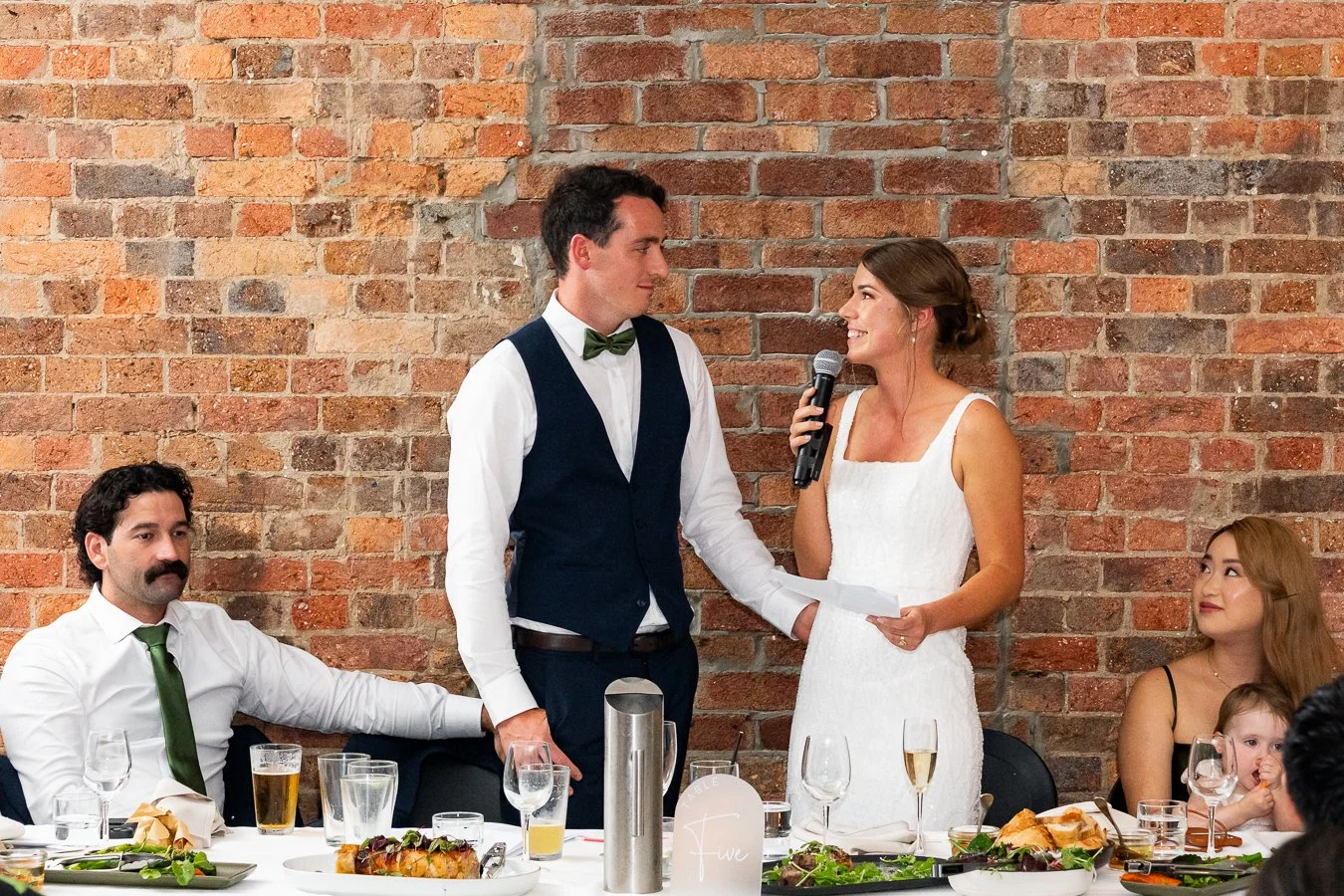 bride Sonya speak on a mic and look at groom Giordan in their speech