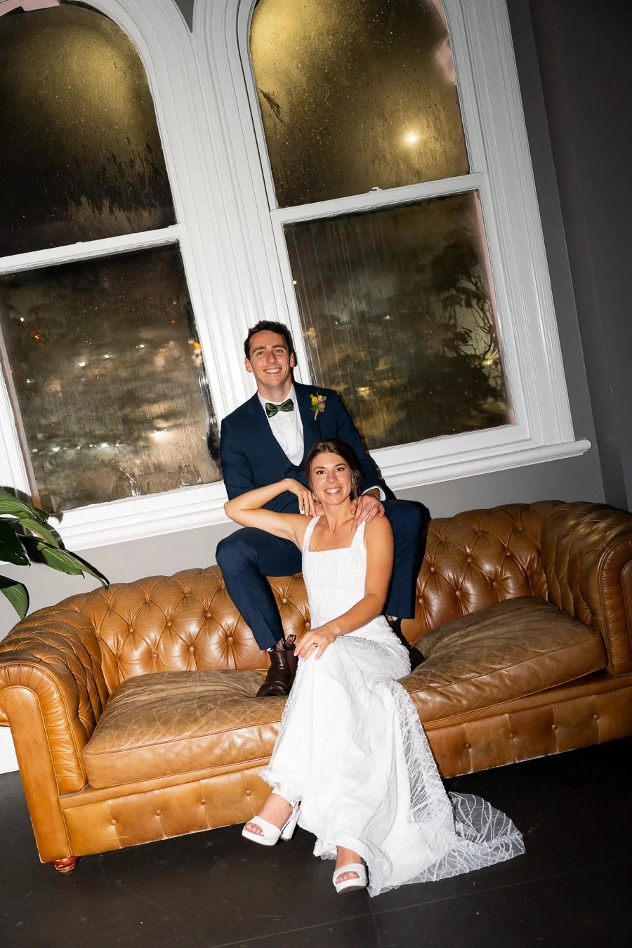 Giordan sitting on the arm of the sofa and Sonya sitting in between with both look at the camera