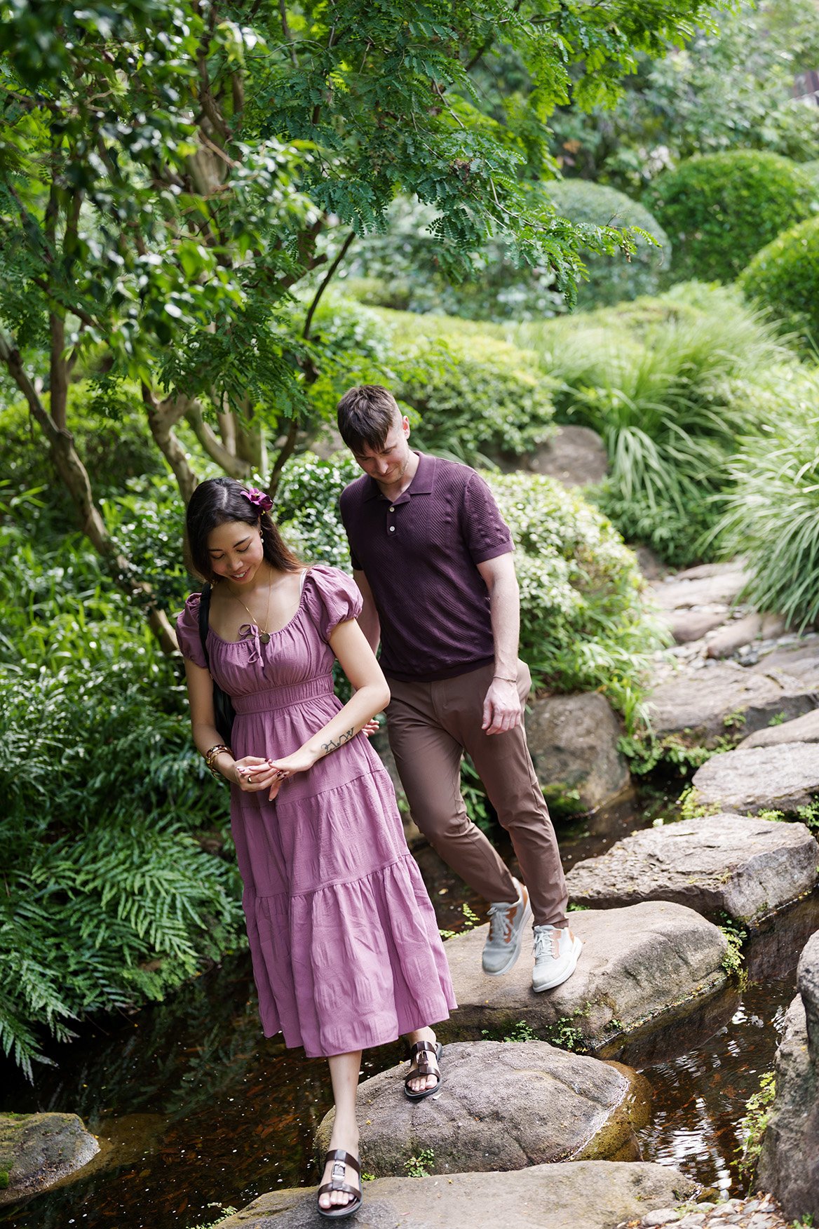 Ruby look at there engagement ring while walking on the rocks, Kyle walking behind her in Brisbane Botanic Gardens Mt Coot-tha