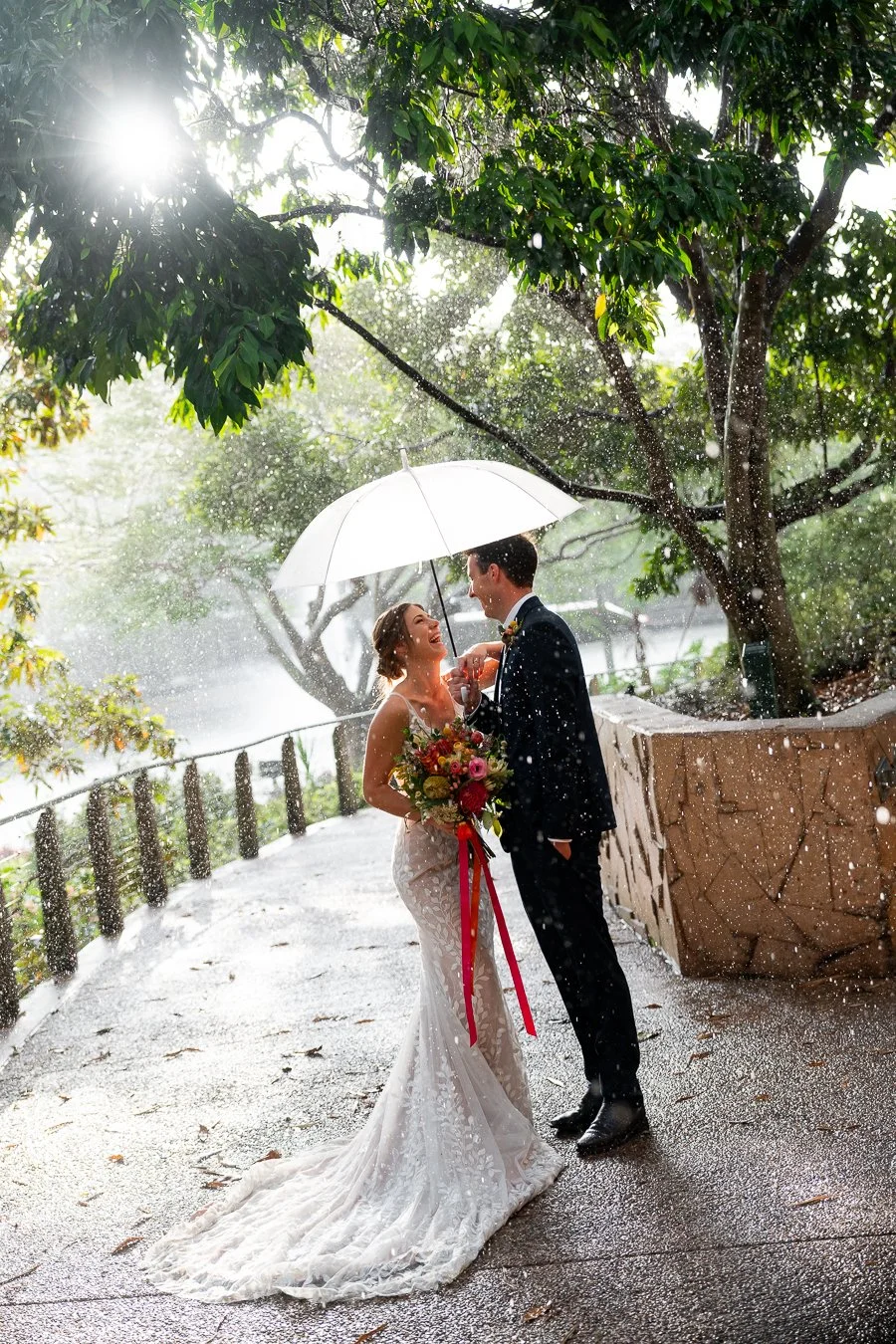Sonya and Giordan holding a white umbrella together with laughter under a sun rain in roma street parkland, captureed by Brisbane wedding photographer Whistler Li