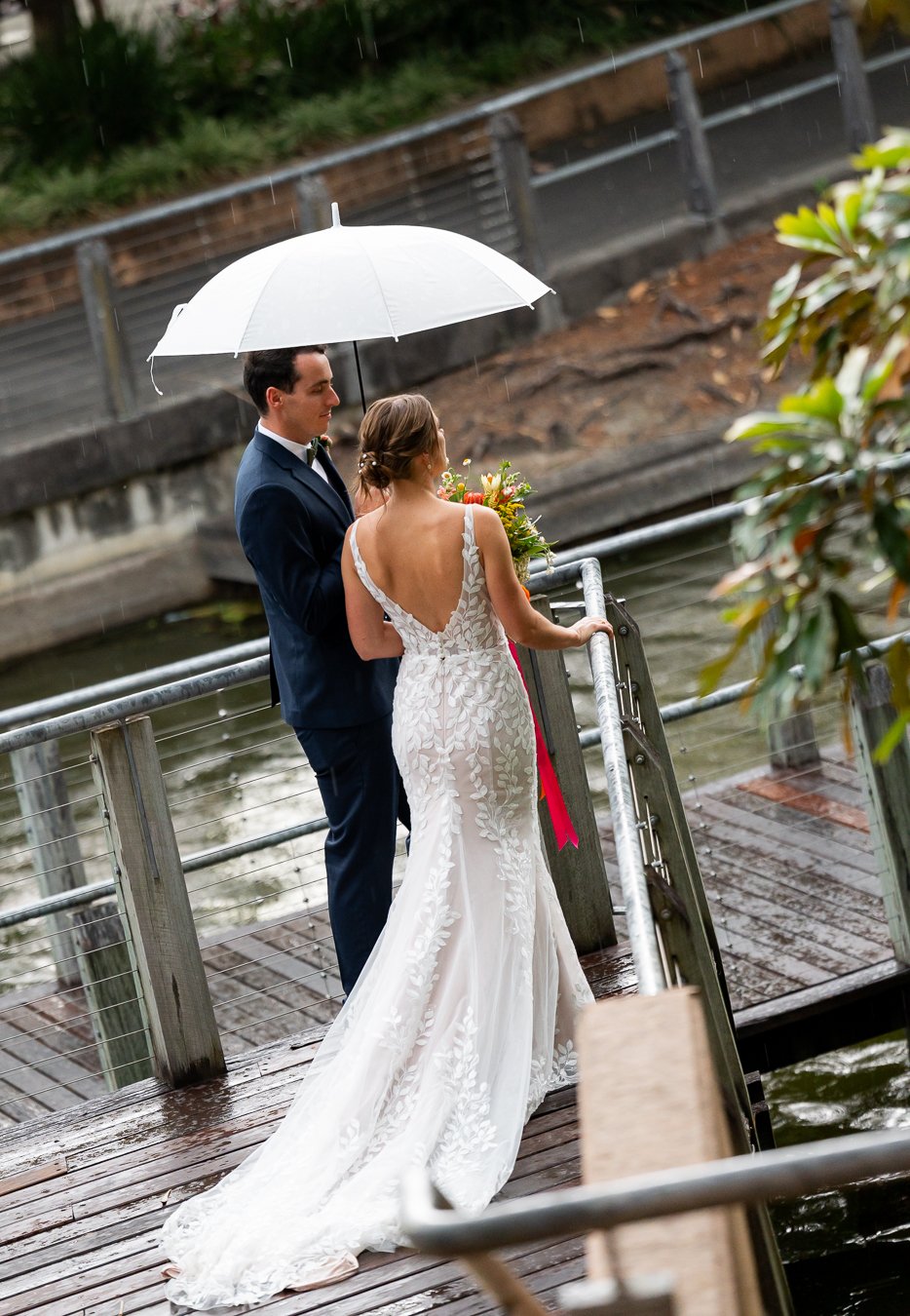 bride holding a rail and groom stand next to her with an umbrella