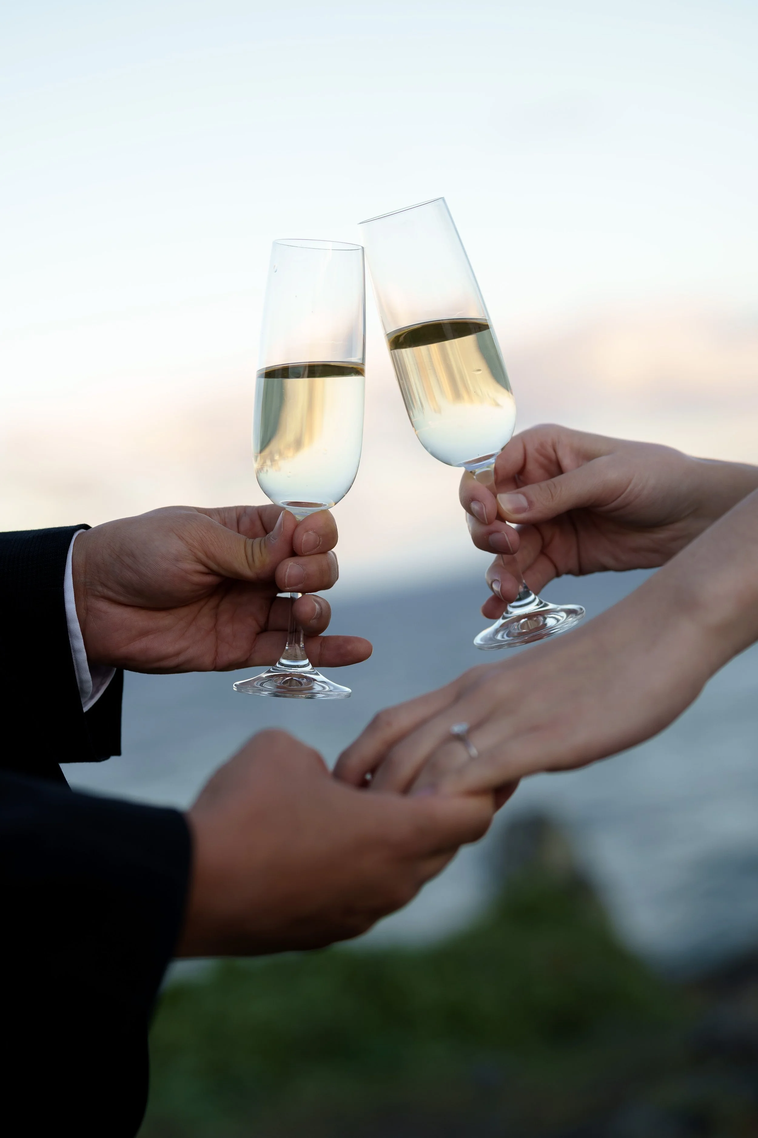 two glasses fill with Champaign click together, and Margaret and Silva's hand holding together with a engagement ring on it