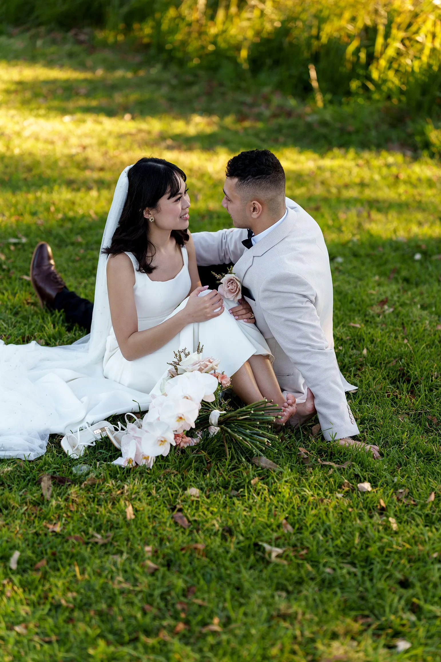 Annecy and Enrique look at each other, candid and playful, barefoot on the grass, golden hour, genuine laughter