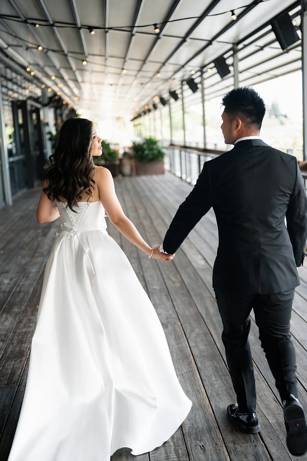 Bride Tiffy and groom Kai holding hands, running away from the camera with the bride looking lovingly at the groom. Their joyful and carefree moment captures the excitement and energy of their wedding day, creating a dynamic and intimate scene filled