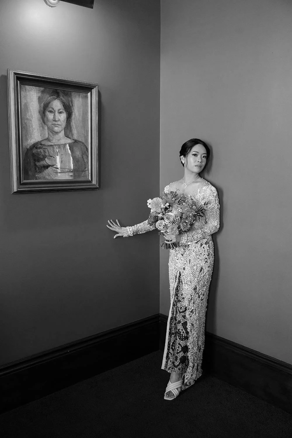 bride Nori leaning on the red wall with one hand touching it, a lady picture on the other side of the wall