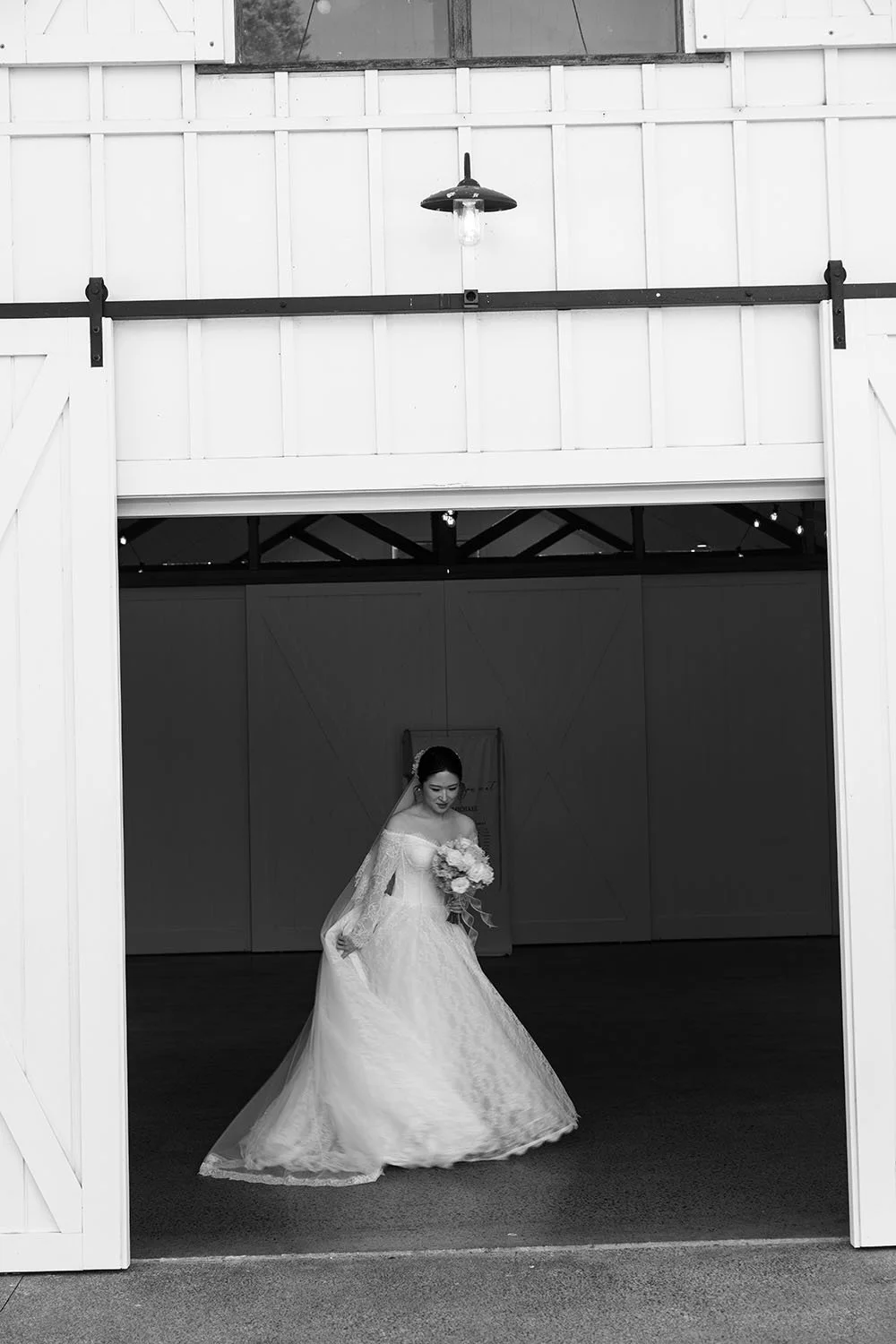 Lisa pull back her wedding dress trail under a barn door
