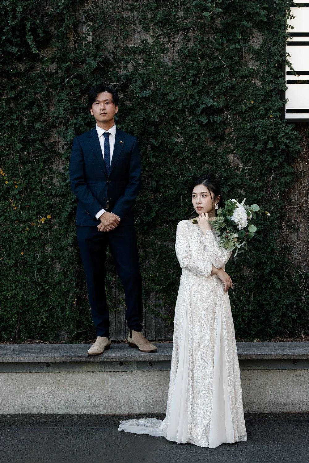 groom Leo stand up on a bench two hands in front and look the Brisbane wedding photographer, bride Cassie standing next to him holding flower