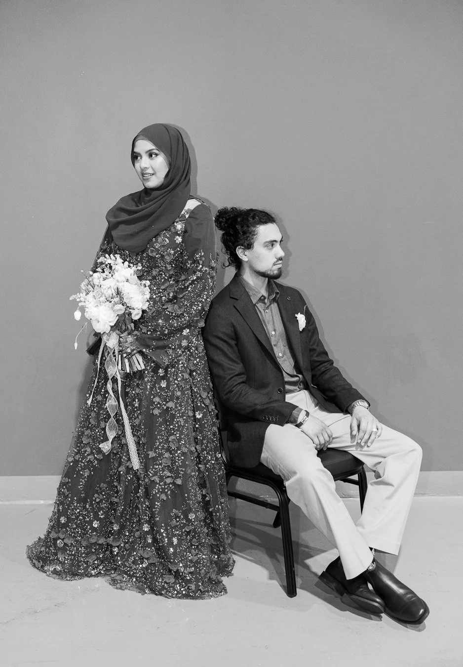 Junaid seating and Afifah standing next to him, and they both look away from the camera