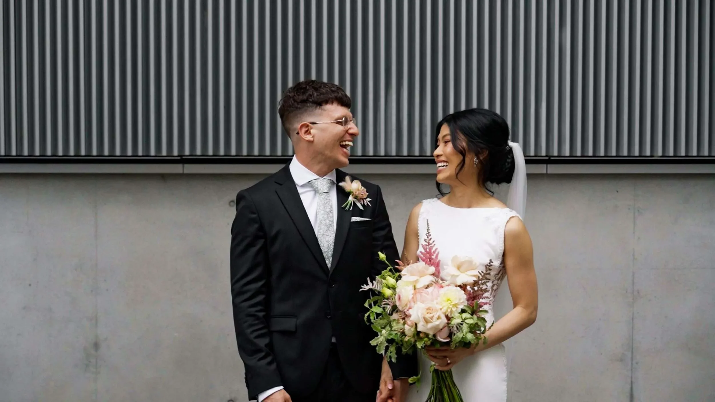 Vy and Fehim look at each other with bid laughing and bride Vy holding a flower