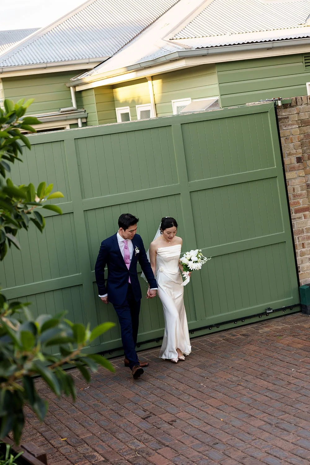 The bride Flora and groom Eric walk hand in hand past a green green doorway, enjoying the moment together