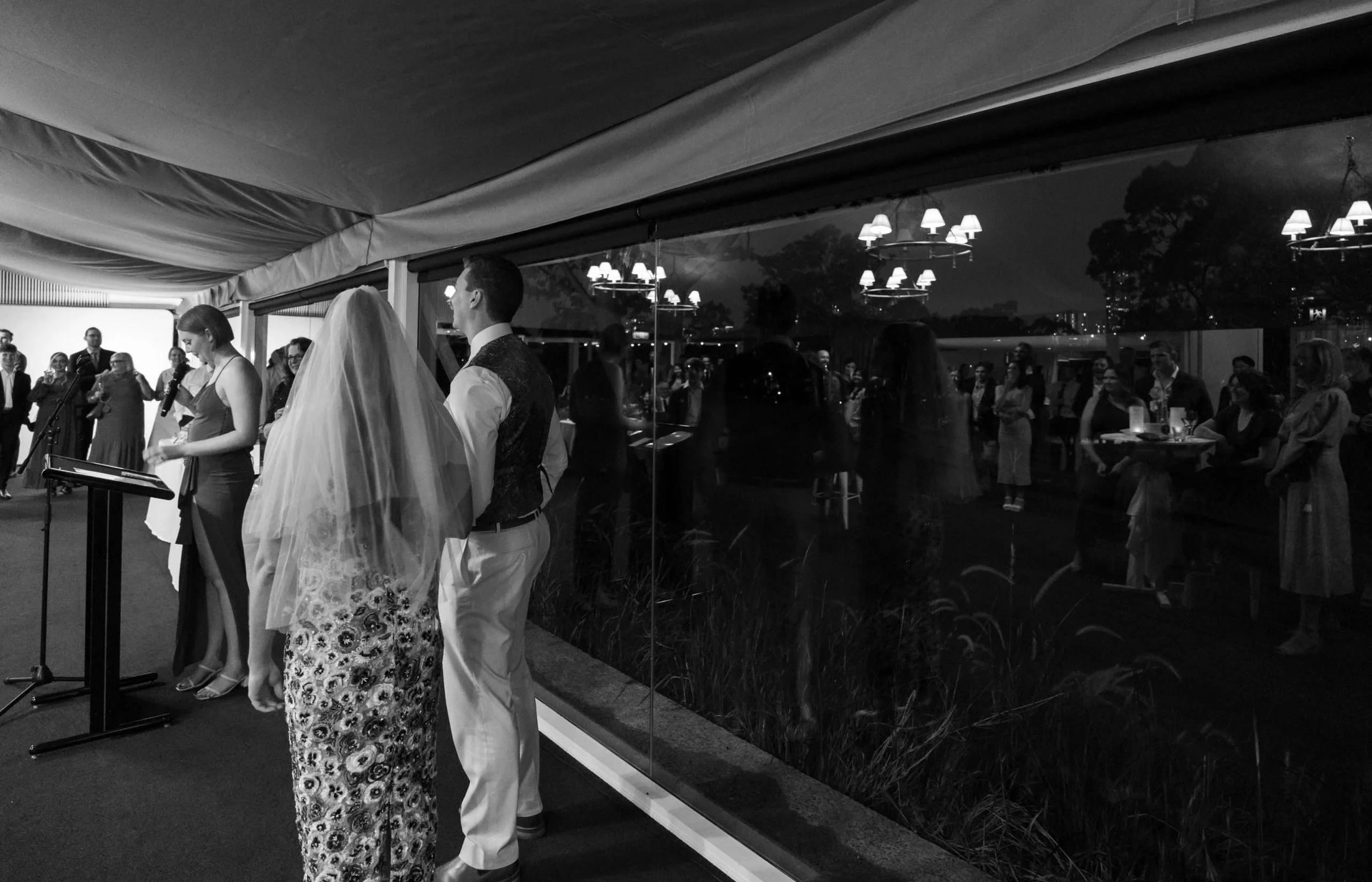 mirror reflection shows all guests stand in the Victoria park garden marquee reception room while groom's sister making a speech