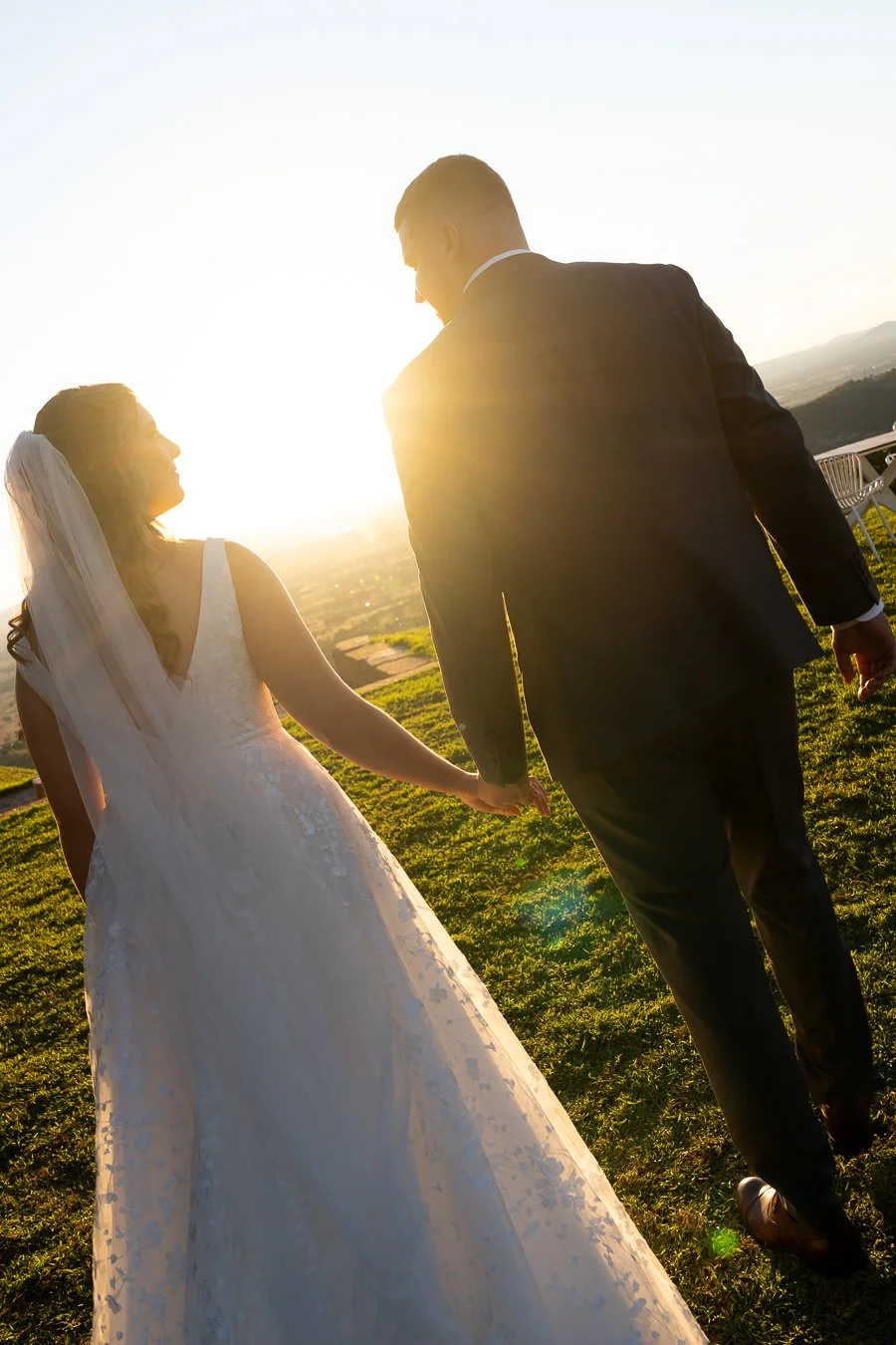 bride and groom holding hands walking towards to the sunset