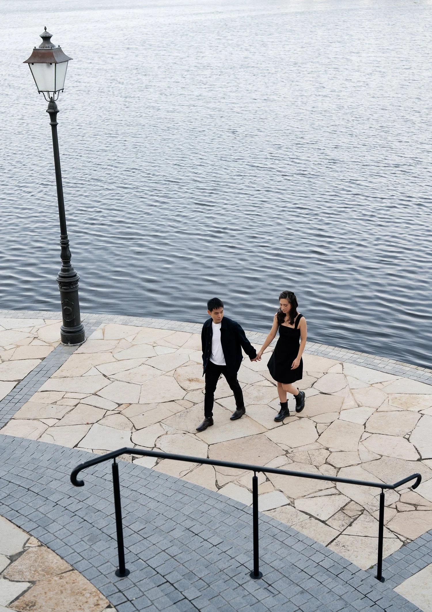 Paul holding Krystel's hand walking towards to the stairs and lake behind them